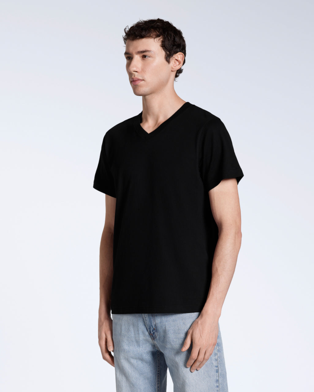 A man looking away from the camera at an angle with his arms by his side, modelling a plain black, organic cotton v neck t shirt.