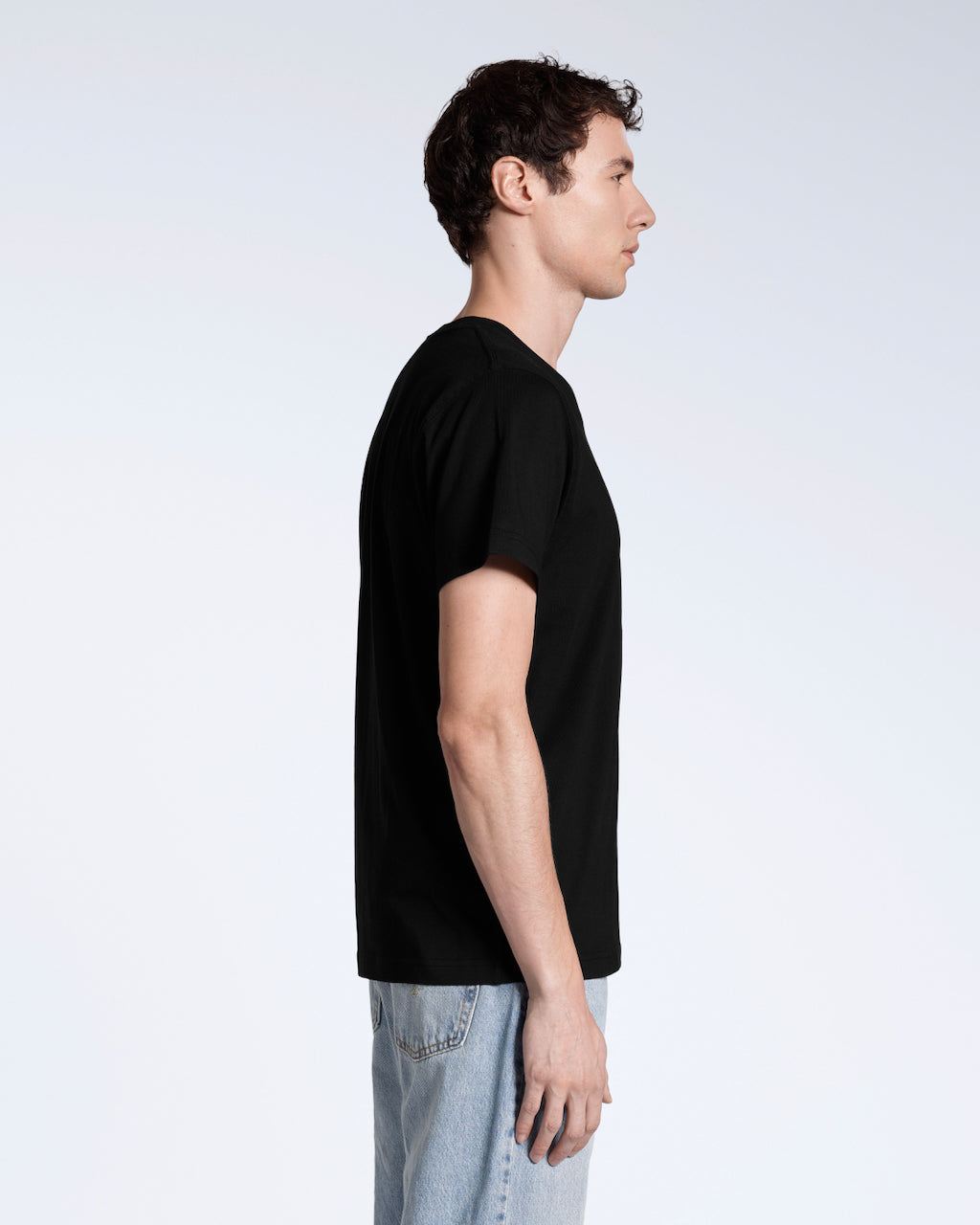 A man facing side on, with his arms by his side, modelling a plain black, organic cotton v neck t shirt.
