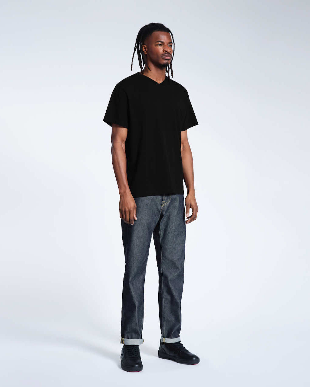 A full body photo of a man looking away from the camera, modelling a plain black organic cotton v neck t shirt.