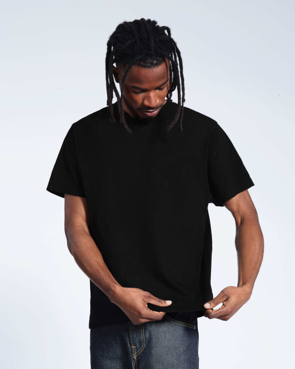 A man looking down and touching the bottom of his plain black organic cotton v neck t shirt.