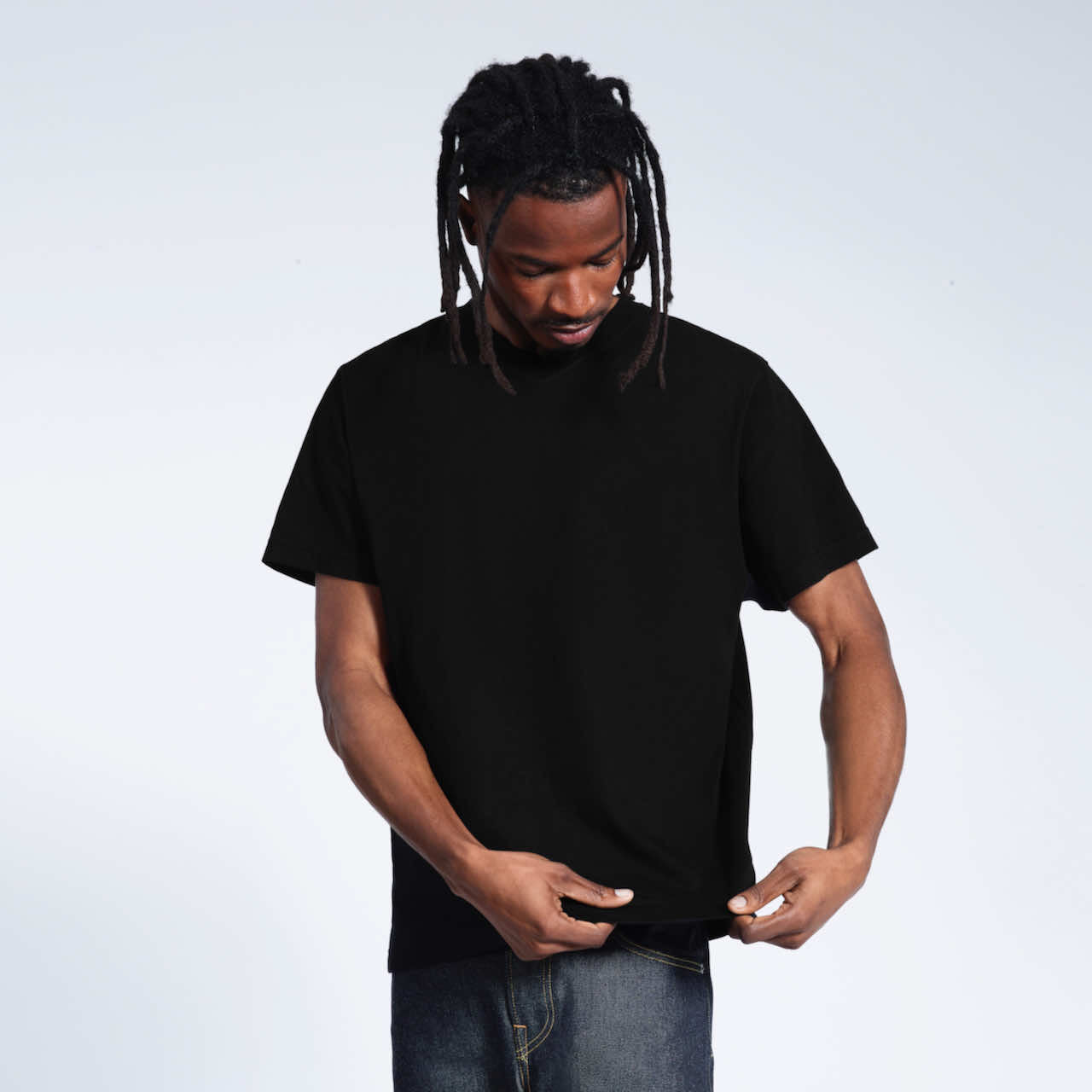 A man looking down and touching the bottom of his plain black organic cotton v neck t shirt.