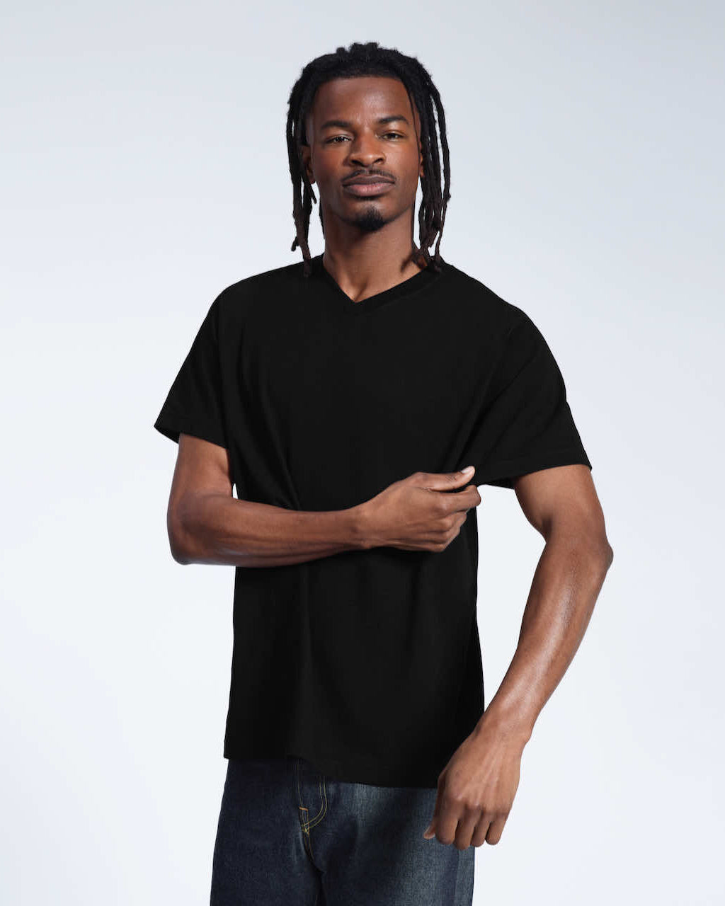 A man looking into the camera and touching his sleeve, modelling a plain black organic cotton v neck t shirt.