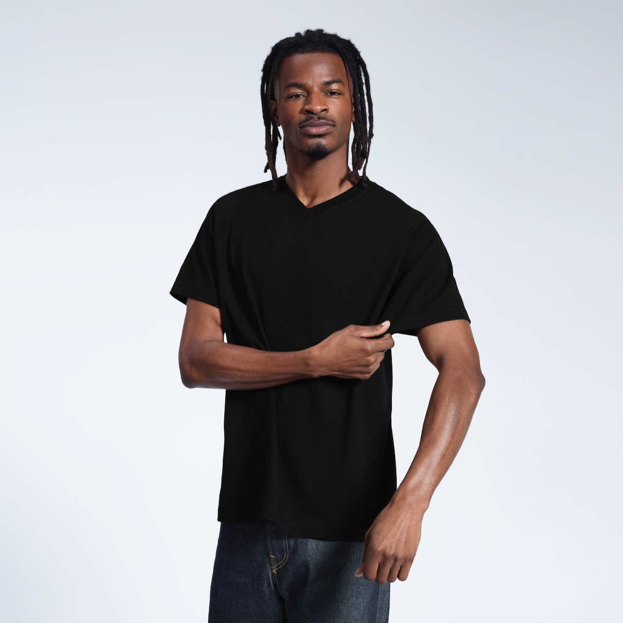 A man looking into the camera and touching his sleeve, modelling a plain black organic cotton v neck t shirt.