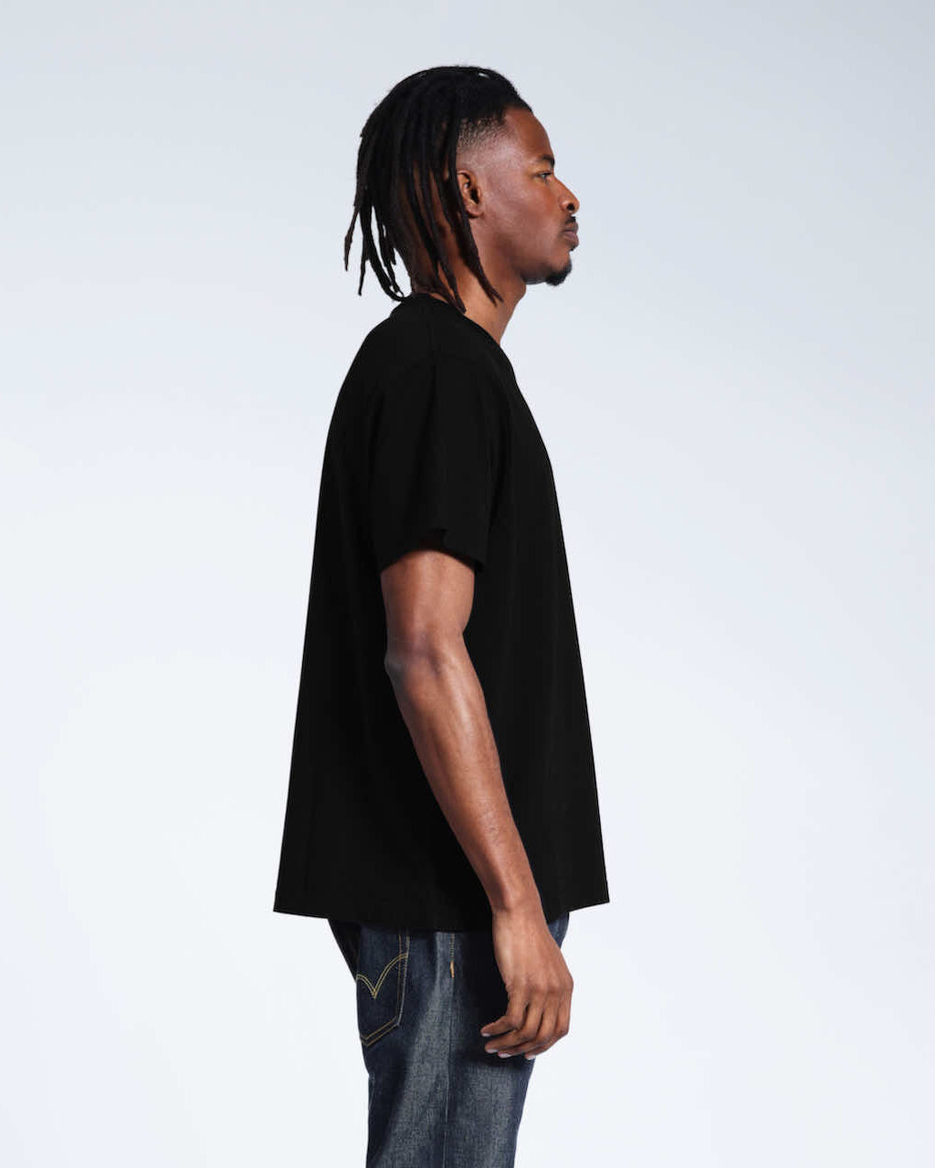 A man facing side on with his arms by his sides, modelling a plain black organic cotton v neck t shirt.