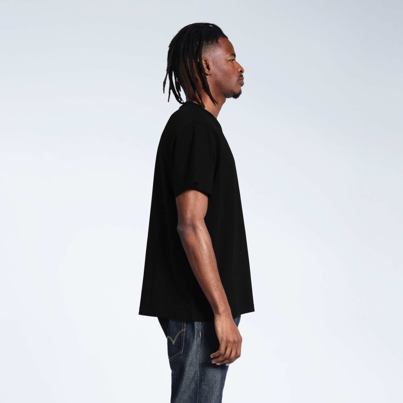 A man facing side on with his arms by his sides, modelling a plain black organic cotton v neck t shirt.