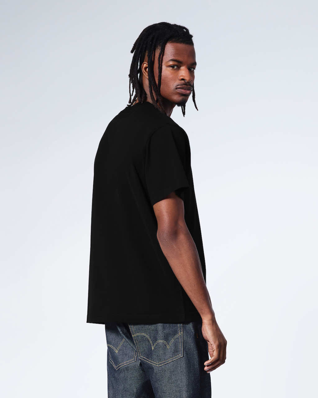 A man turned to look at the camera, showing the back of his plain black organic cotton v neck t shirt.