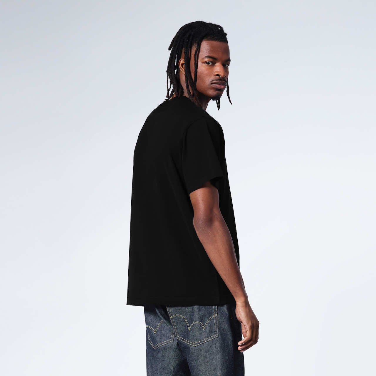 A man turned to look at the camera, showing the back of his plain black organic cotton v neck t shirt.
