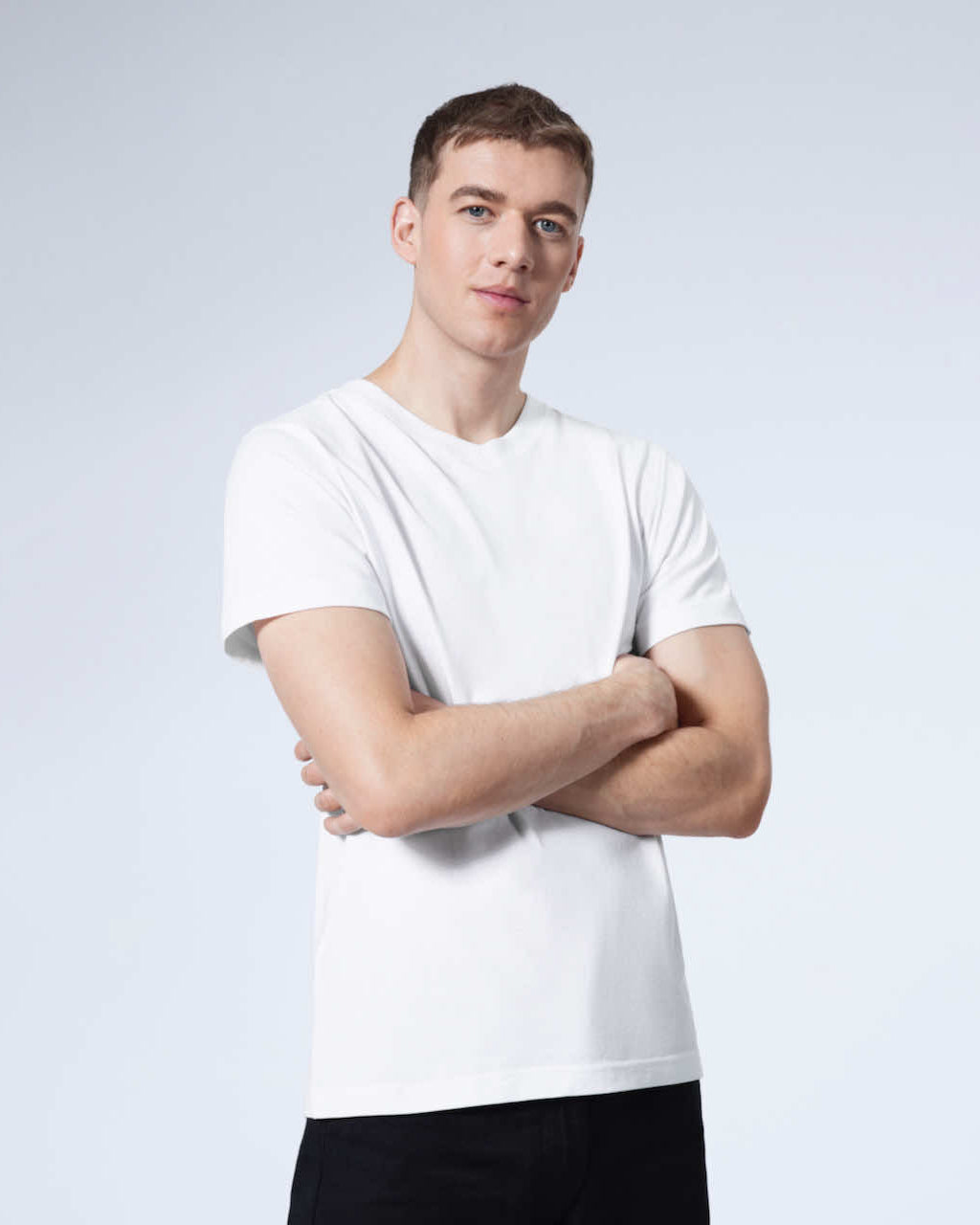 A man looking into the camera with his arms folded, modelling a plain white organic cotton v neck t shirt.