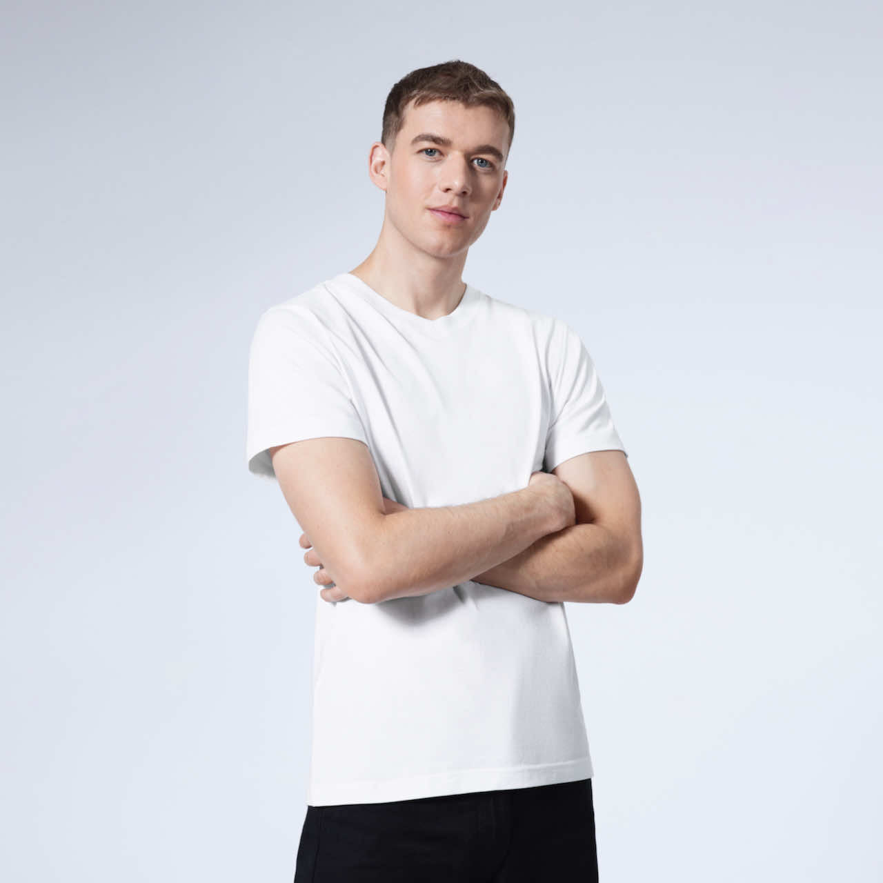 A man looking into the camera with his arms folded, modelling a plain white organic cotton v neck t shirt.