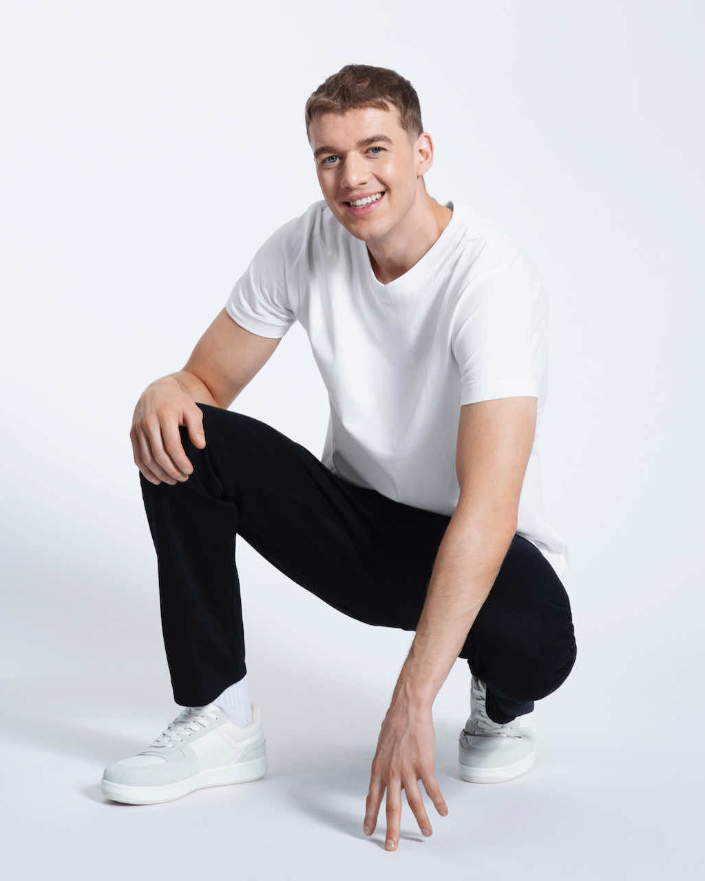 A man crouching down smiling, modelling a plain white organic cotton v neck t shirt.