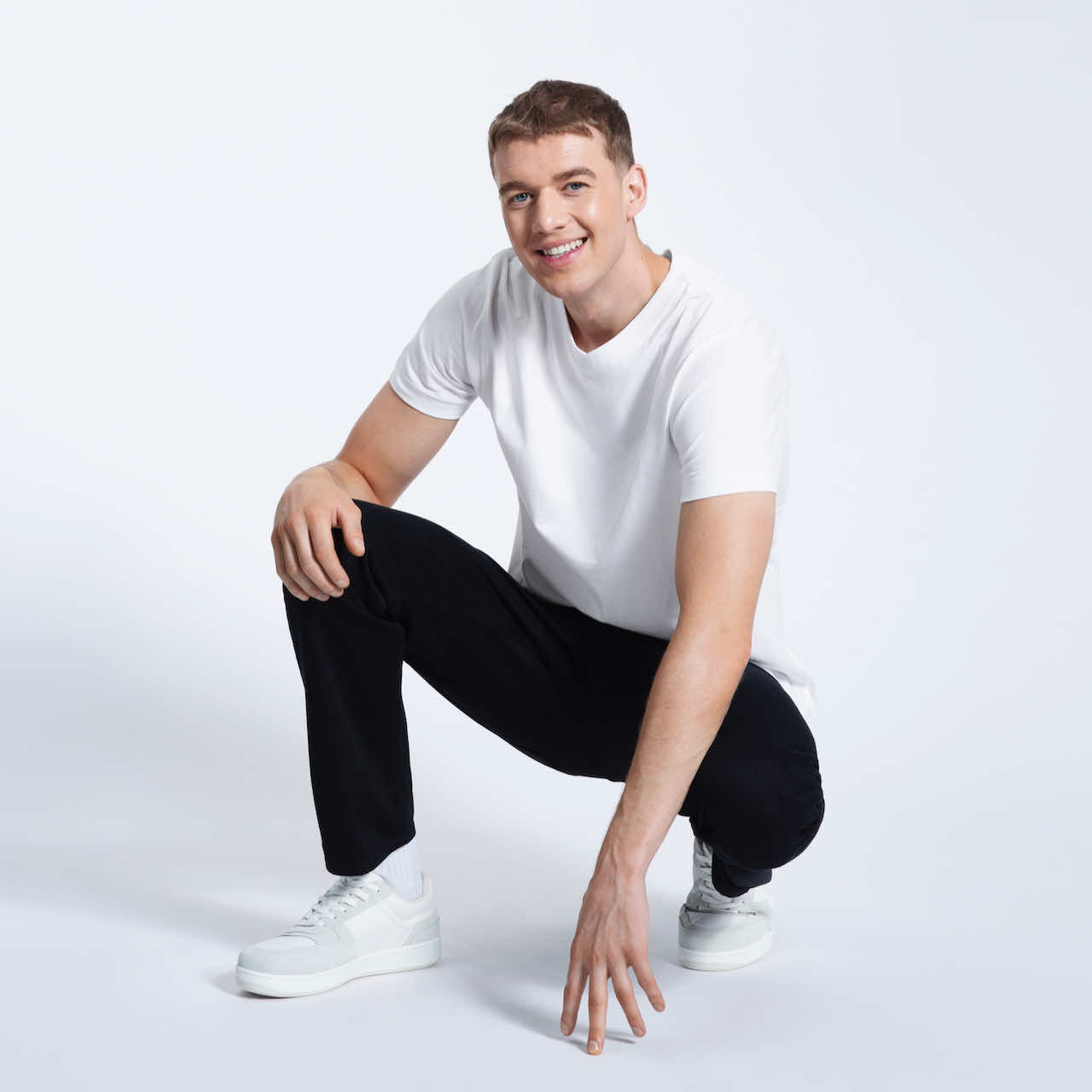 A man crouching down smiling, modelling a plain white organic cotton v neck t shirt.