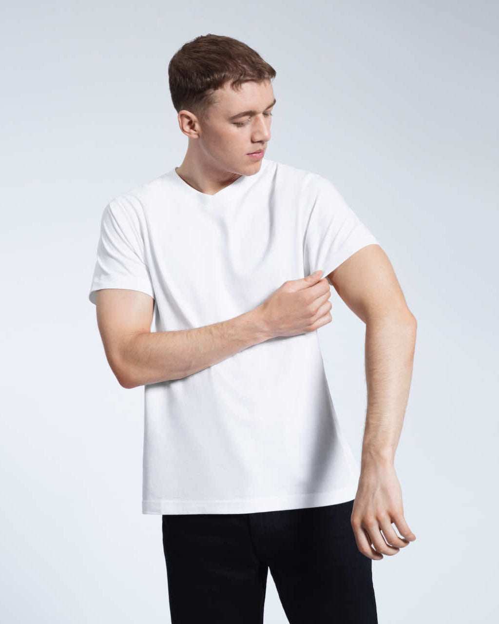 A man looking down and touching his sleeve, modelling a plain white organic cotton v neck t shirt.