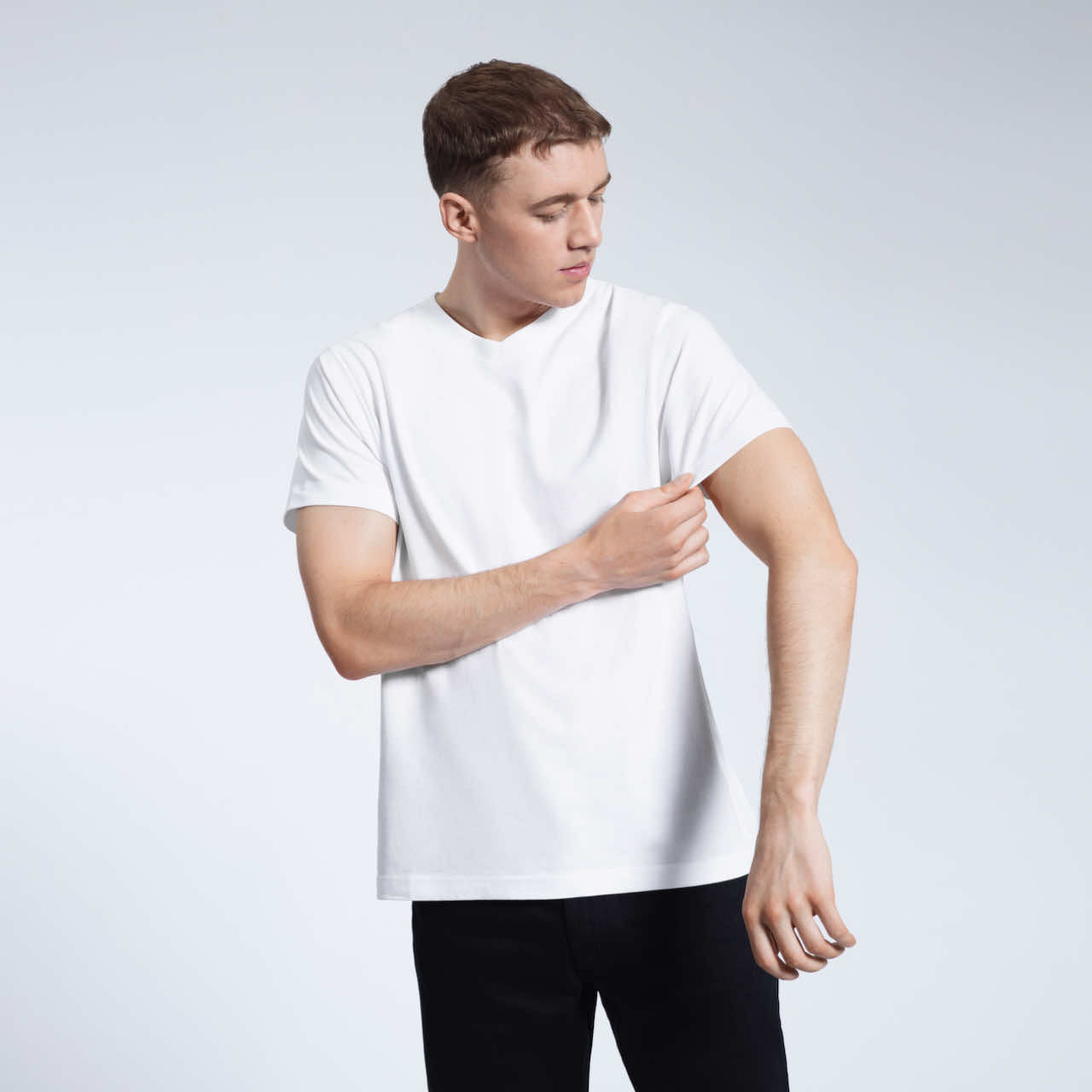 A man looking down and touching his sleeve, modelling a plain white organic cotton v neck t shirt.