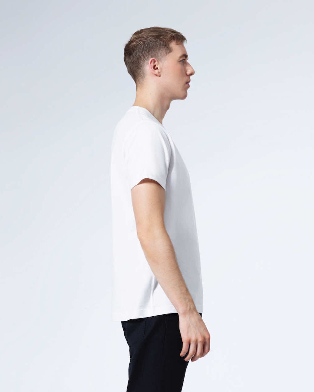 A man facing side on with his arms by his sides, modelling a plain white organic cotton v neck t shirt.