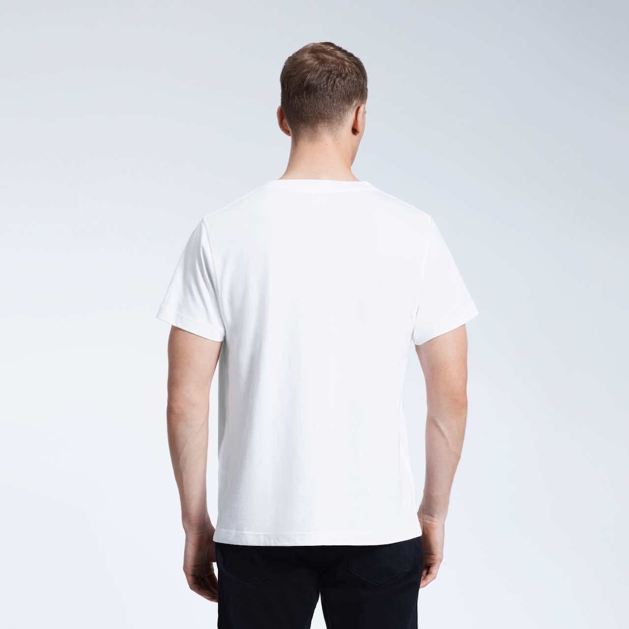 A man facing away from the camera with his arms by his sides, modelling a plain white organic cotton v neck t shirt.