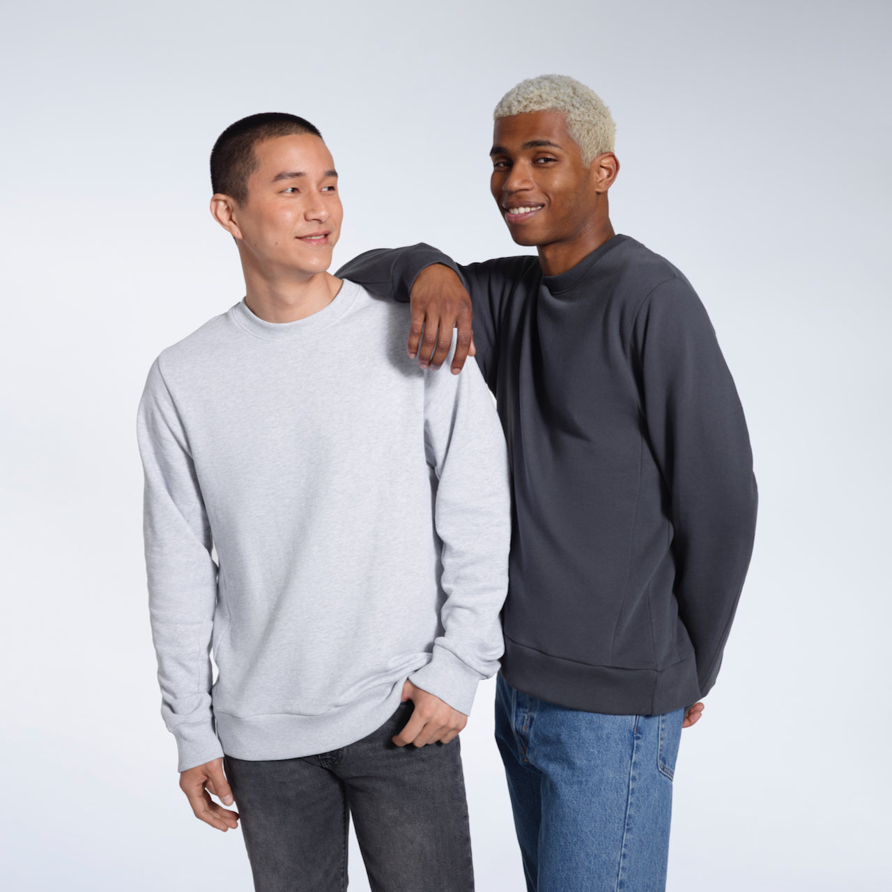 Two men smiling, modelling plain grey and dark grey organic cotton sweatshirts.