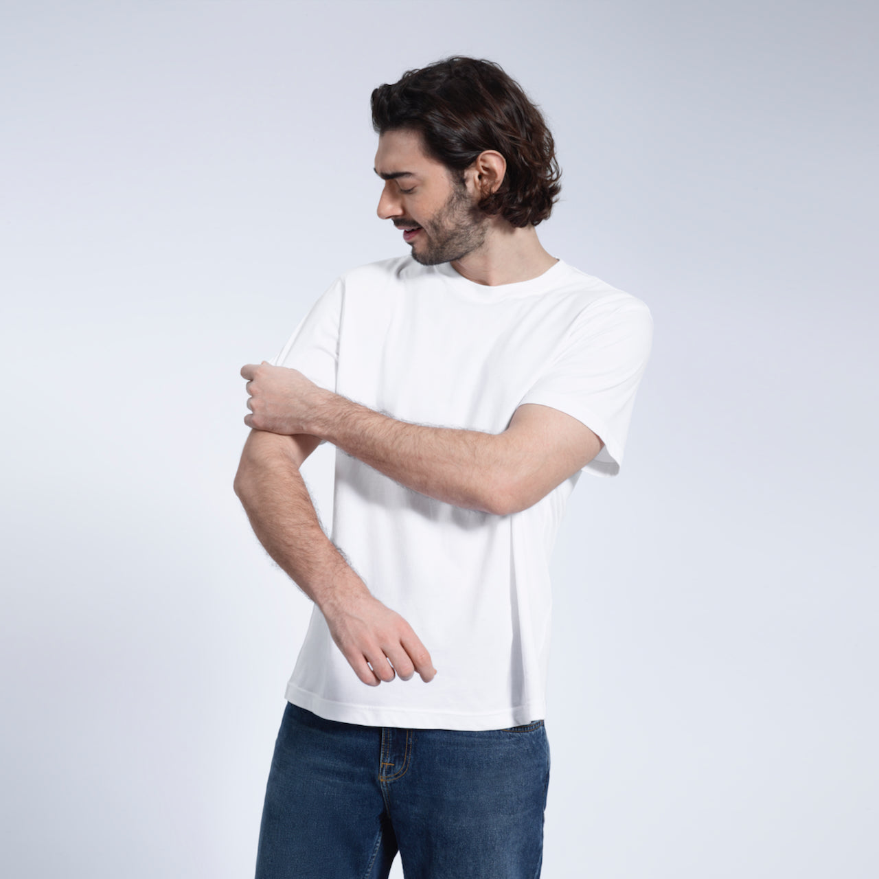A man looking down and touching his sleeve, modelling a plain white short sleeve organic cotton t shirt.