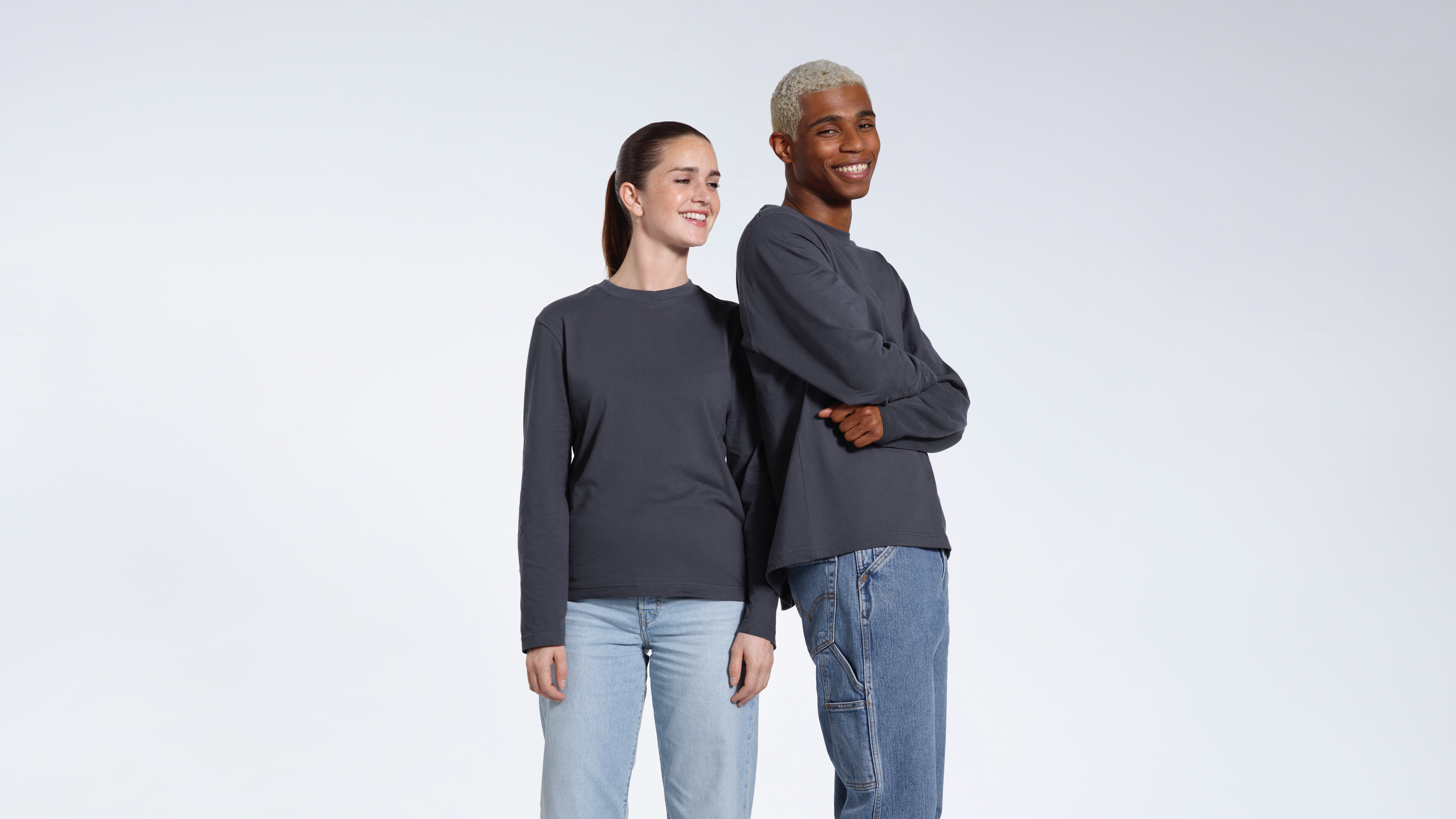 A man and woman smiling, modelling matching plain dark grey long sleeve organic cotton t shirts.