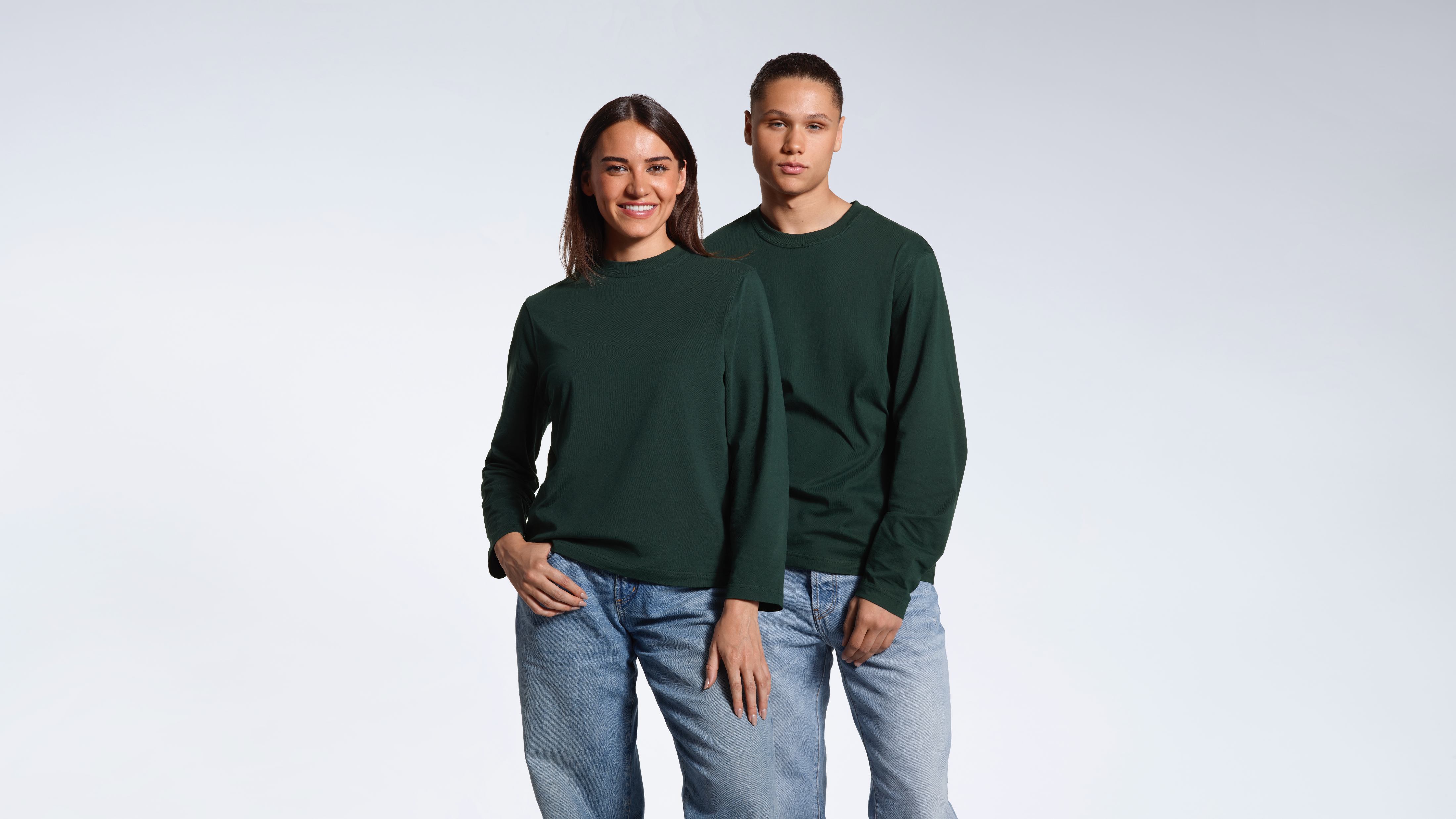 A man and woman looking into the camera, modelling matching plain green long sleeve organic cotton t shirts.