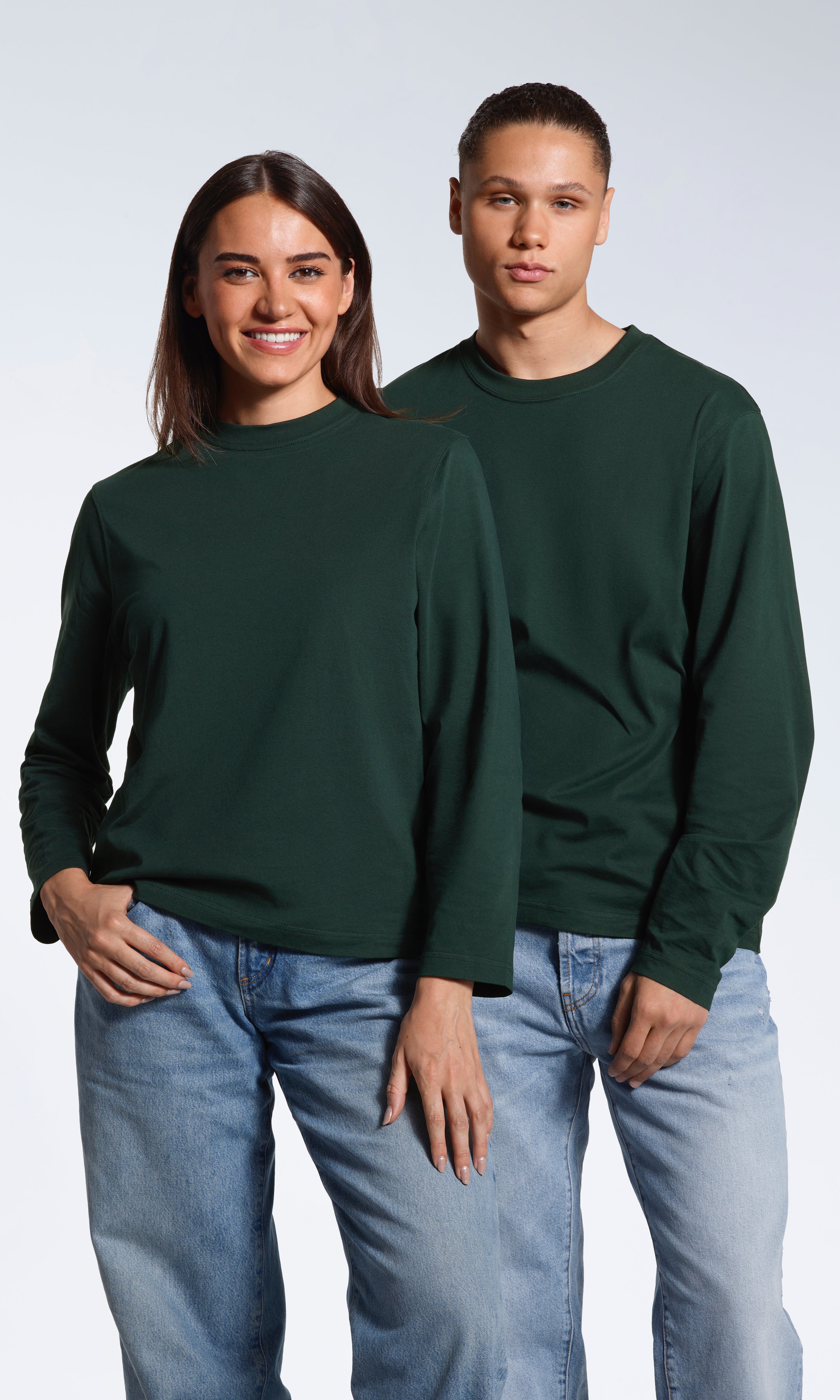 A man and woman looking into the camera, modelling matching plain green long sleeve organic cotton t shirts.