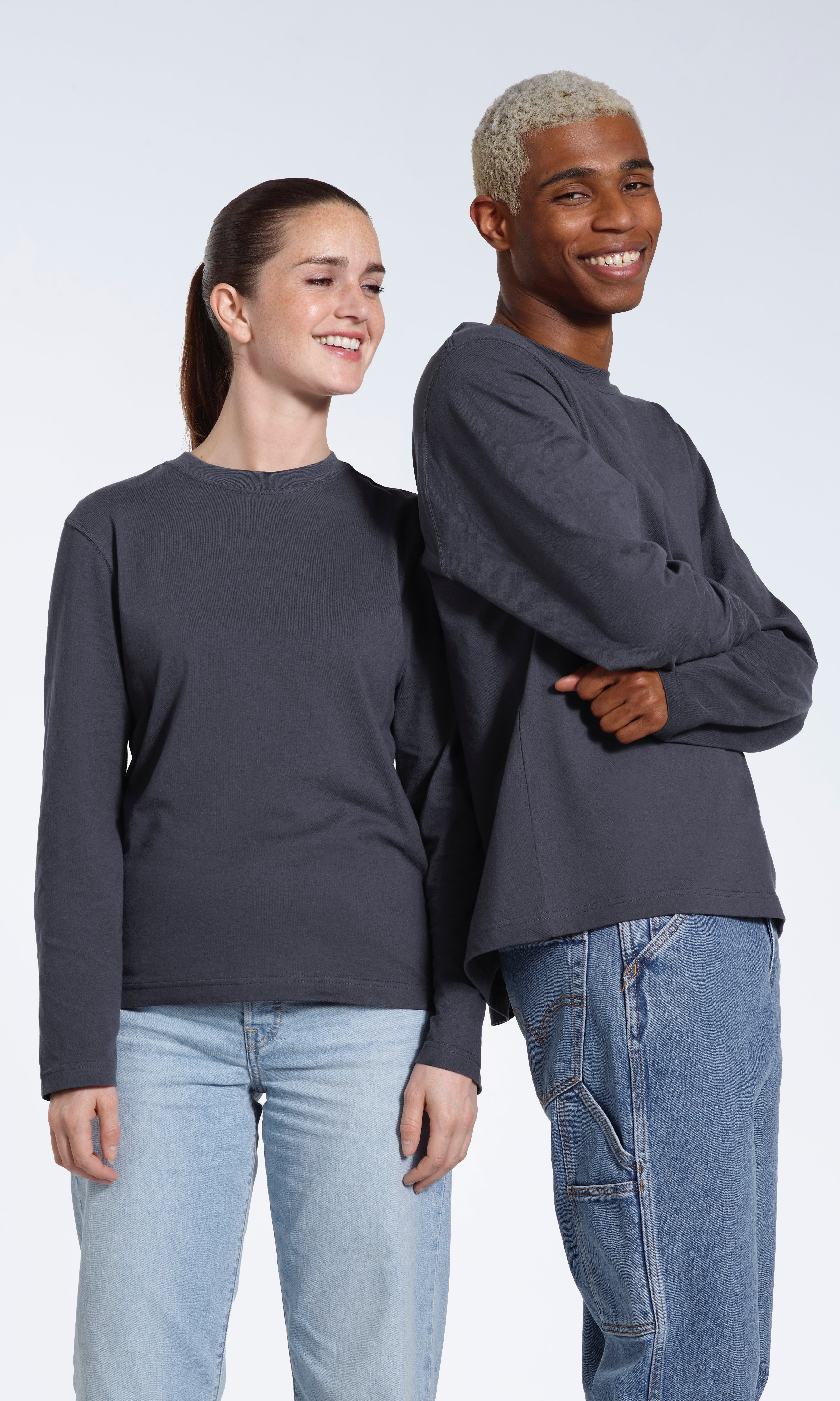A man and woman smiling, modelling matching plain dark grey long sleeve organic cotton t shirts.