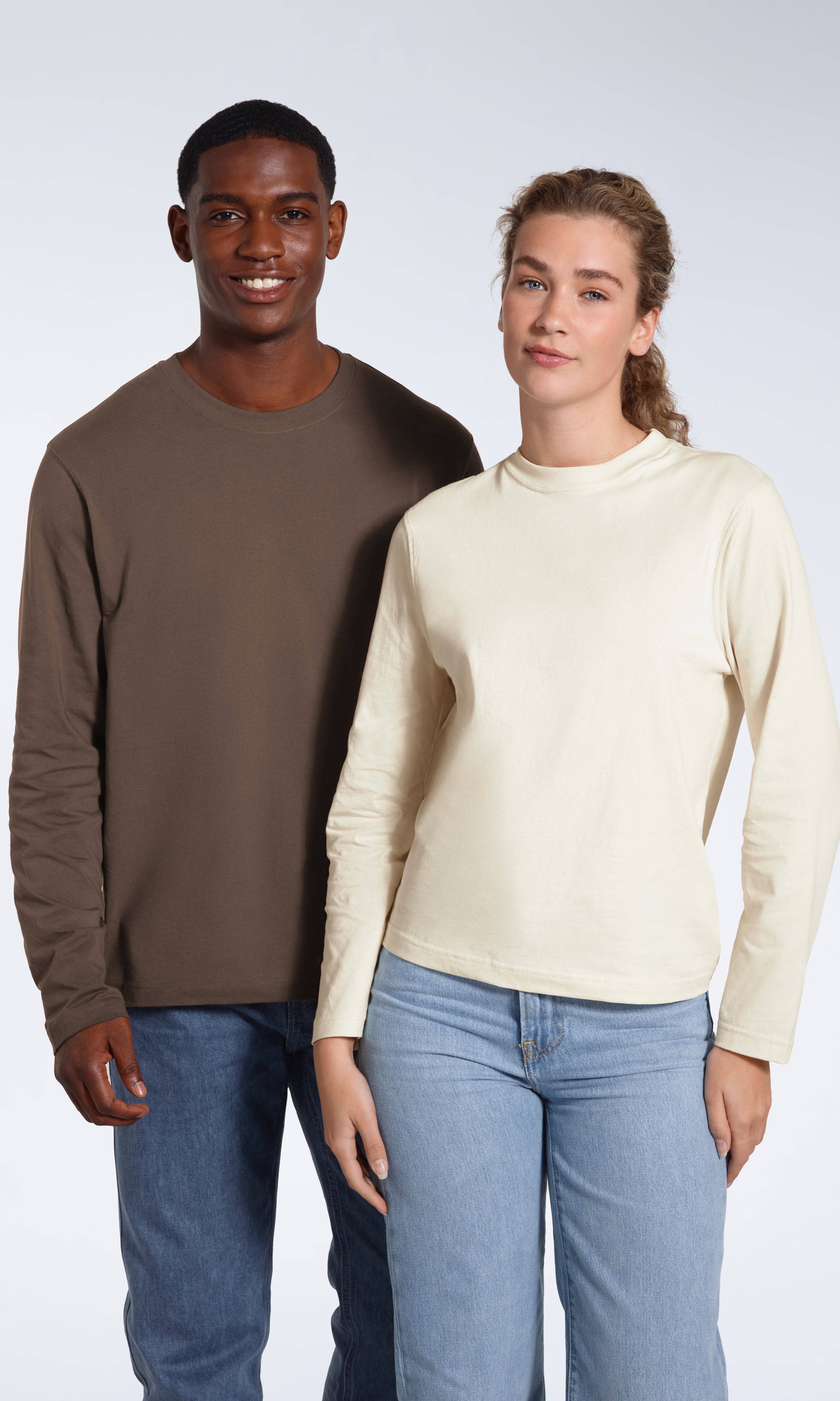 A man and woman smiling into the camera, modelling plain dark khaki and ecru coloured long sleeve t shirts.