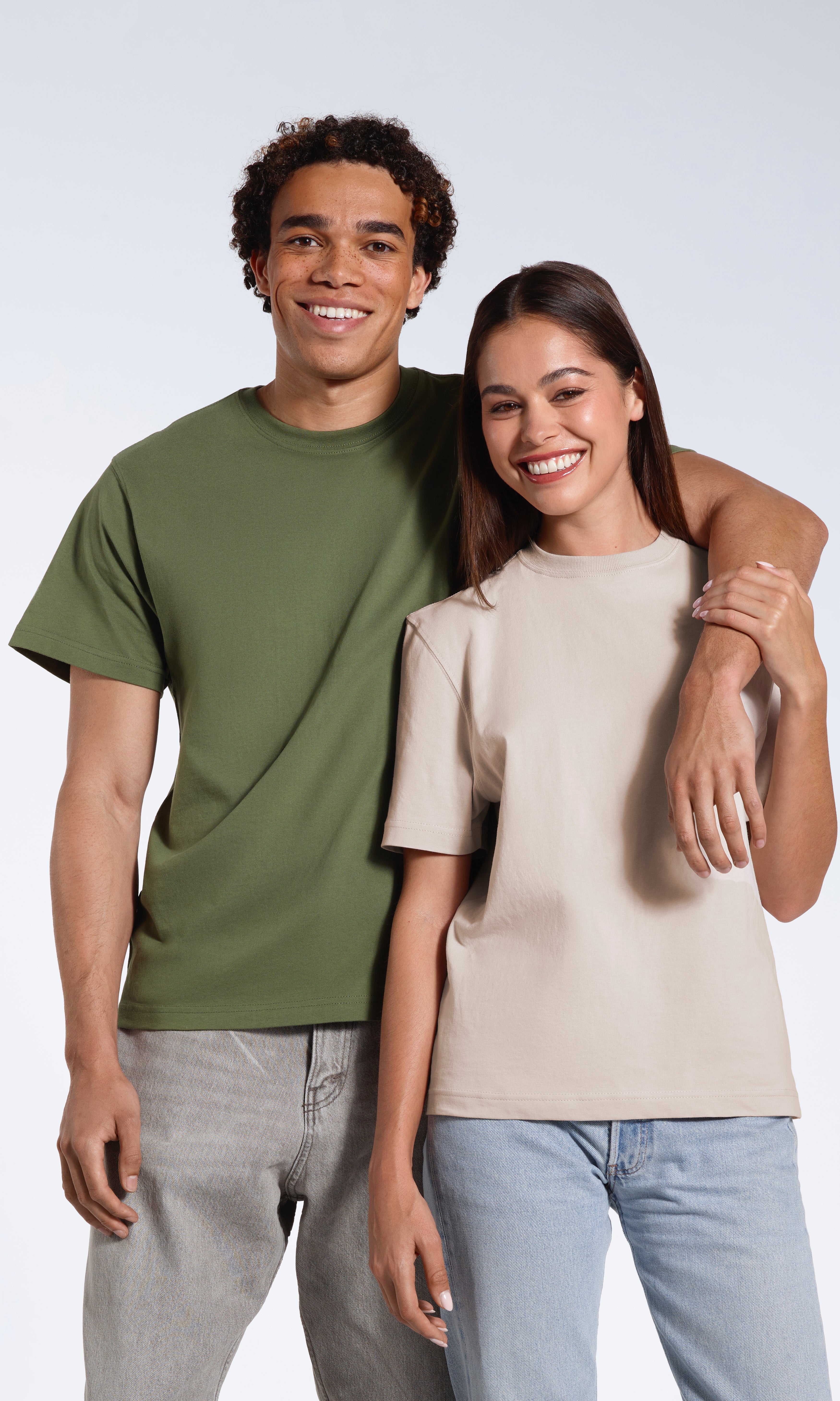 A man with his arm round the woman's shoulder, both smiling into the camera, modelling plain khaki green and stone coloured organic cotton t shirts.
