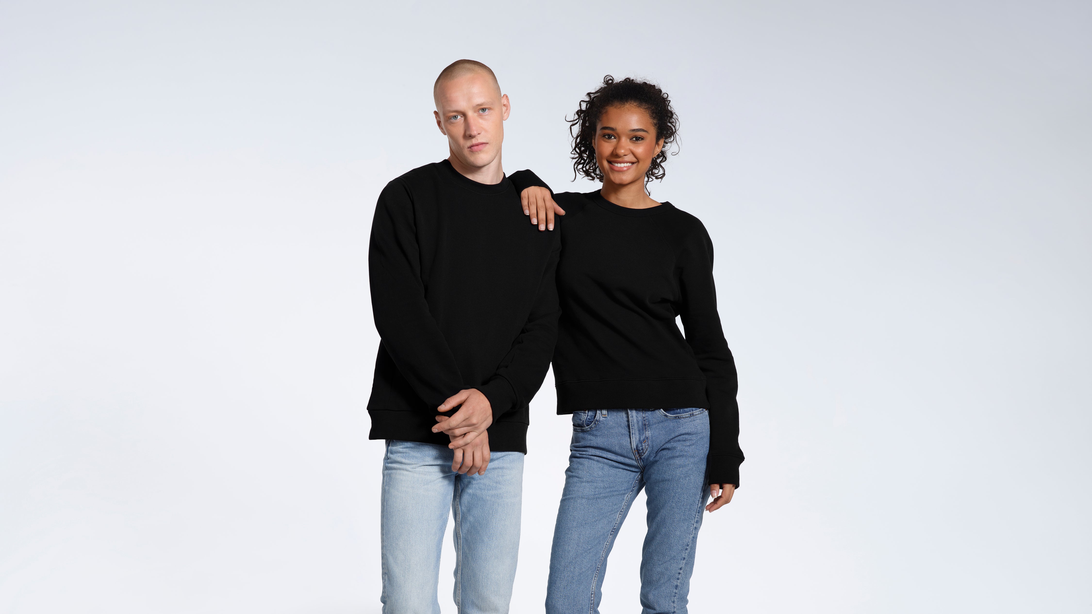 A woman with her hand on the man's shoulder, oth looking into the camera modelling plain black, organic cotton sweatshirts.