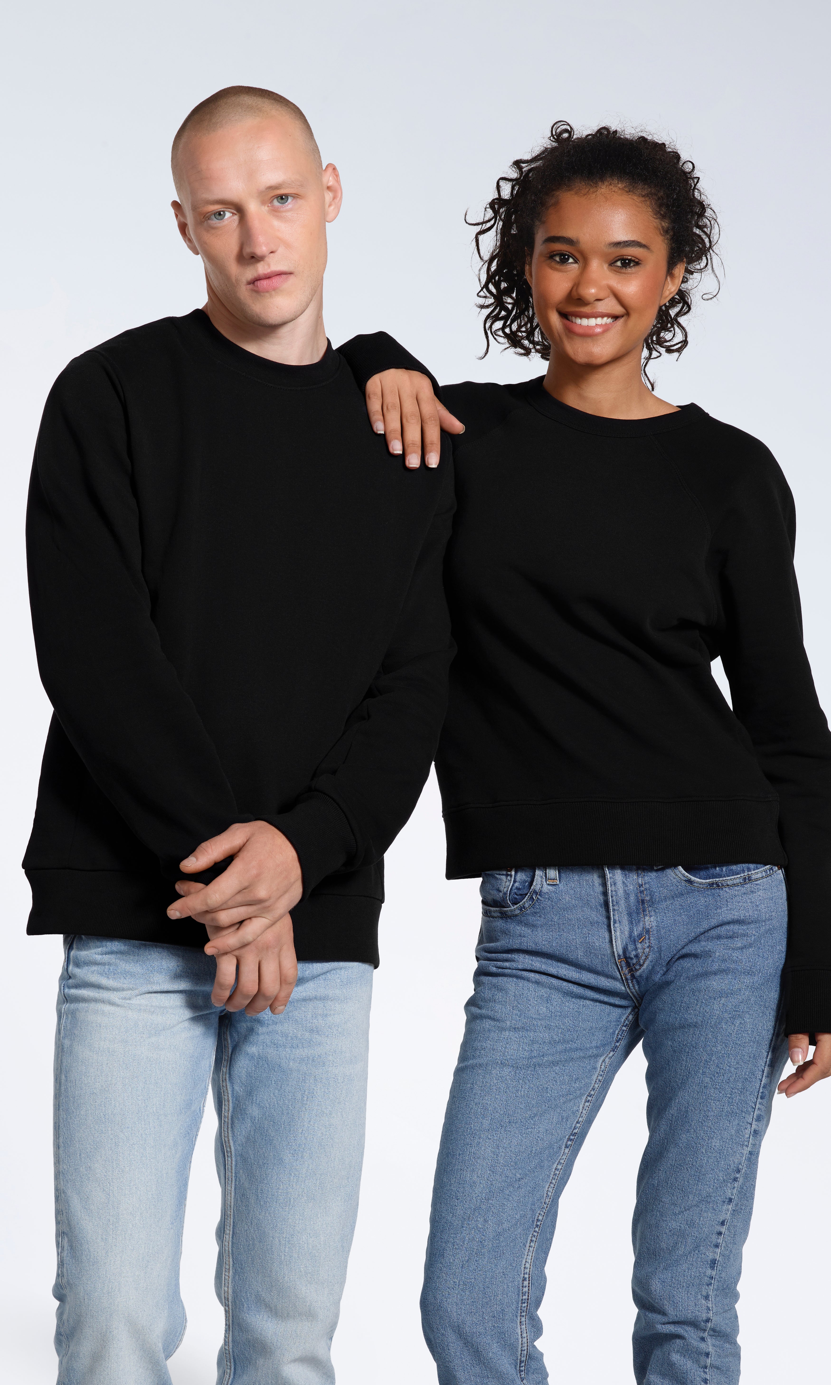 A woman with her hand on the man's shoulder, oth looking into the camera modelling plain black, organic cotton sweatshirts.