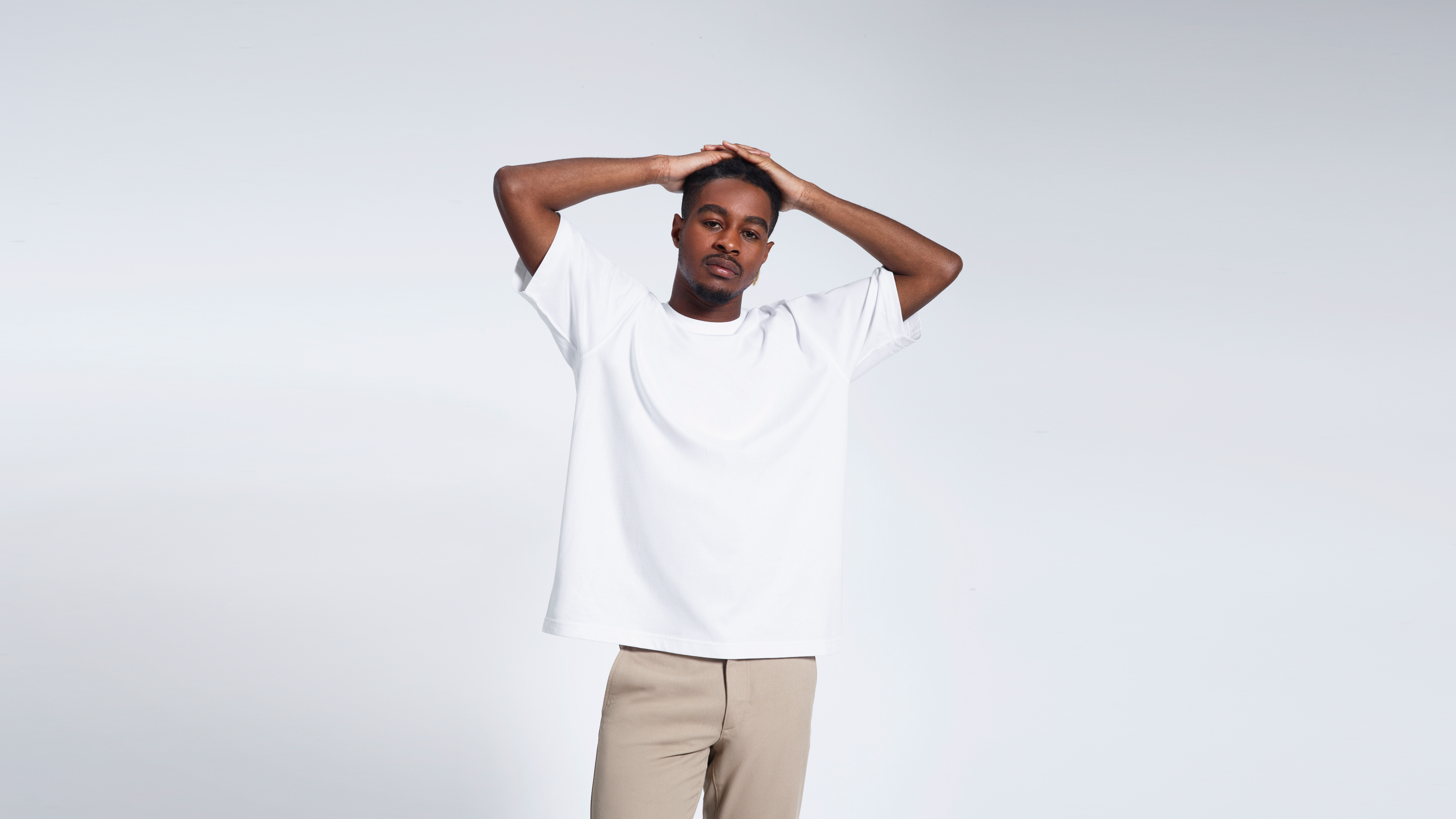 A man looking into the camera with his hands on his head, modelling a white, oversized, heavyweight organic cotton t shirt.