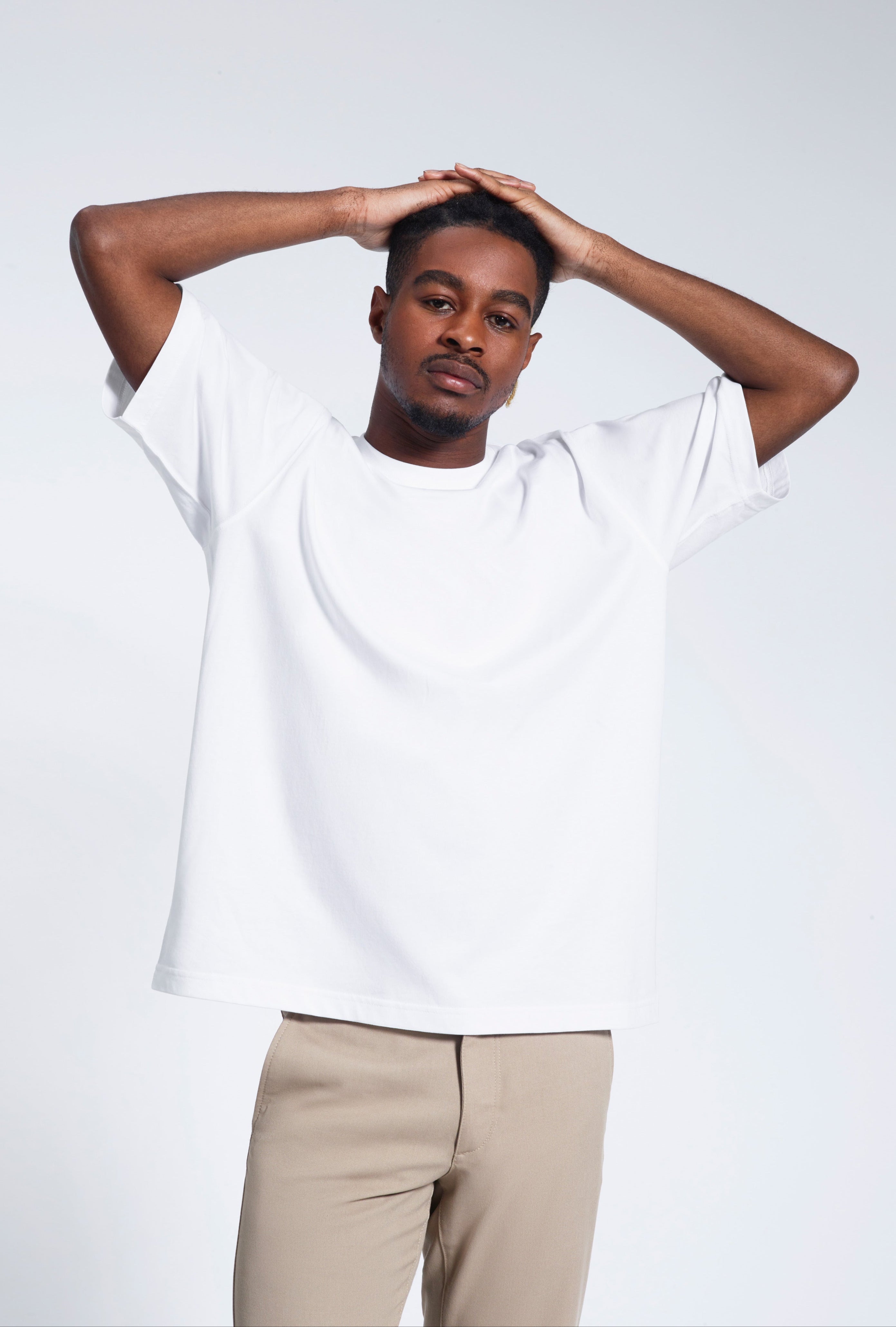 A man looking into the camera with his hands on his head, modelling a white oversized heavyweight organic cotton t shirt.