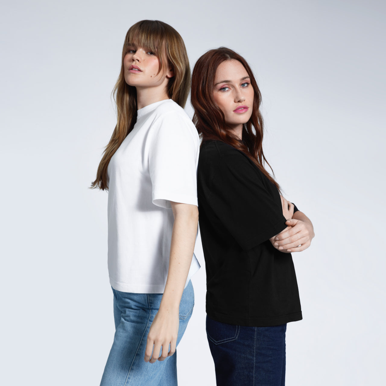 Two women back to back, modelling heavyweight organic cotton boxy, oversized plain white and black short sleeve t shirts.