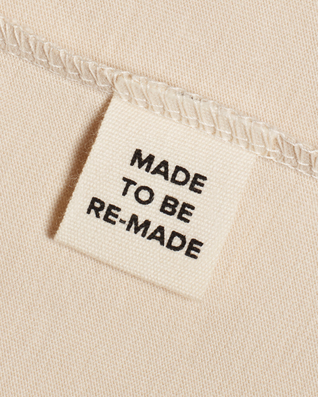 A close up of a label tag in a beige organic cotton t shirt that says 'made to be re made'.