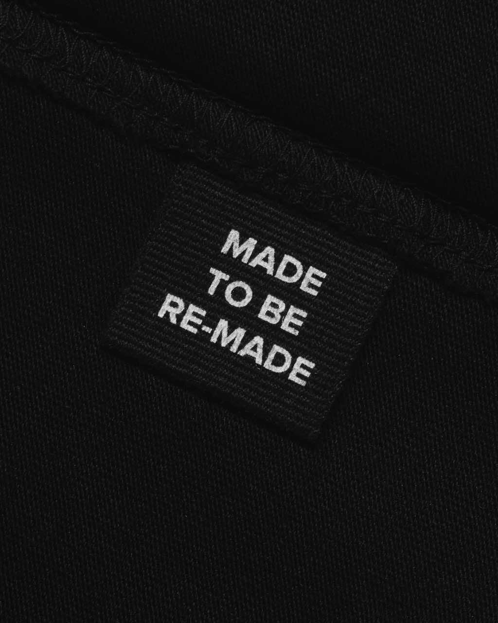 A close up of a label tag in a black organic cotton t shirt that says 'made to be re made'.