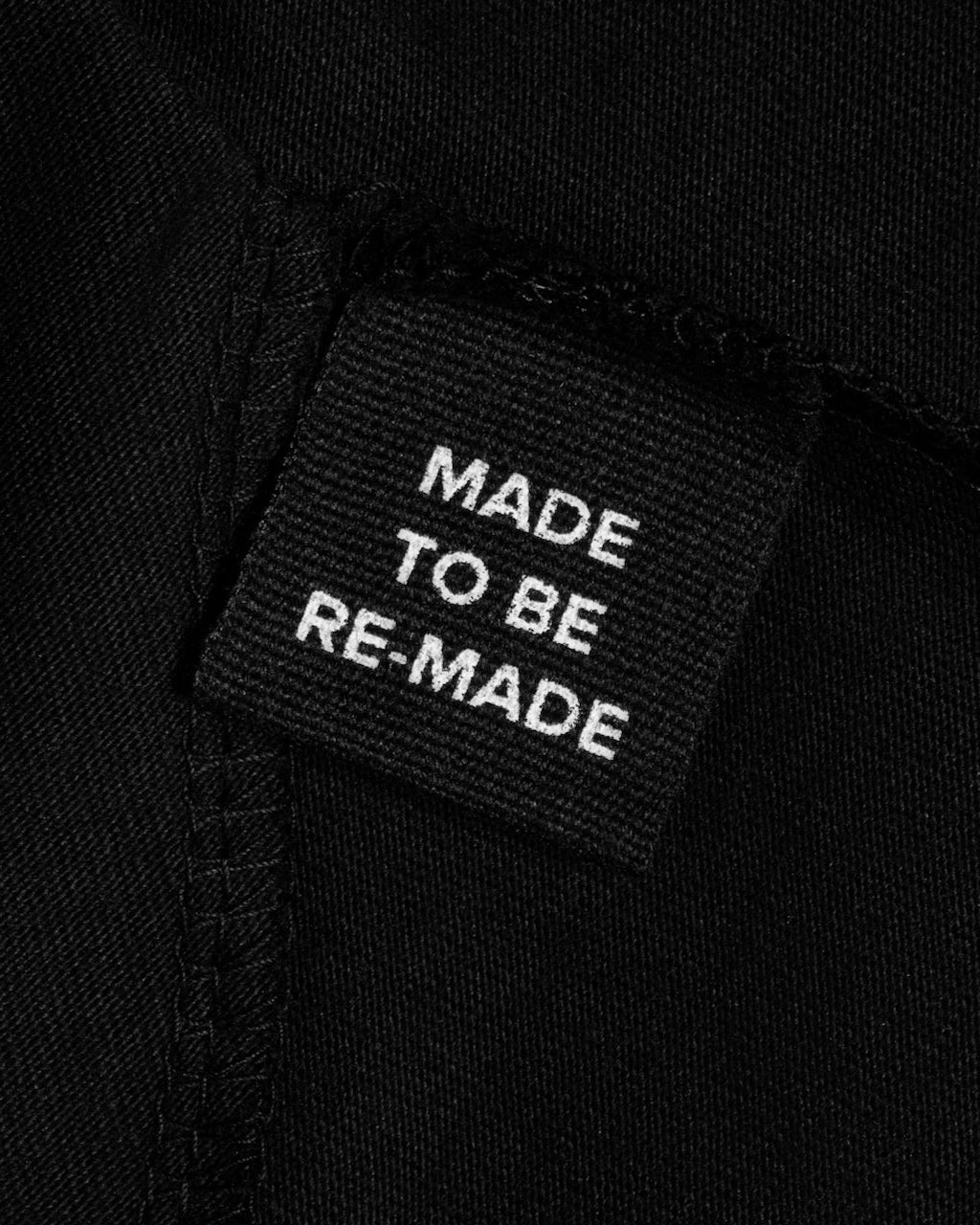 A close up of a label tag in a black organic cotton t shirt dress that says 'made to be re made'.