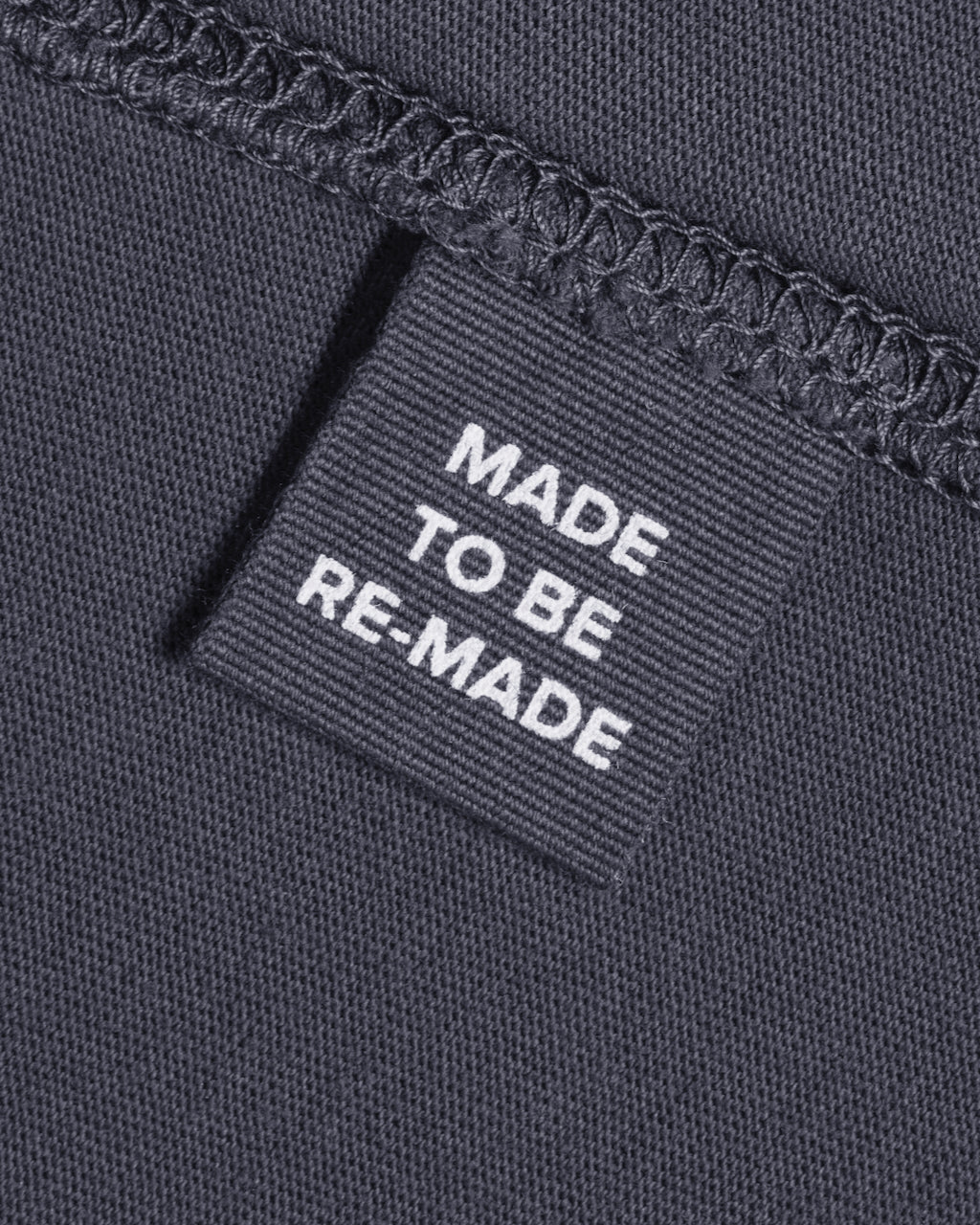 A close up of a label tag in a dark grey organic cotton t shirt that says 'made to be re made'.