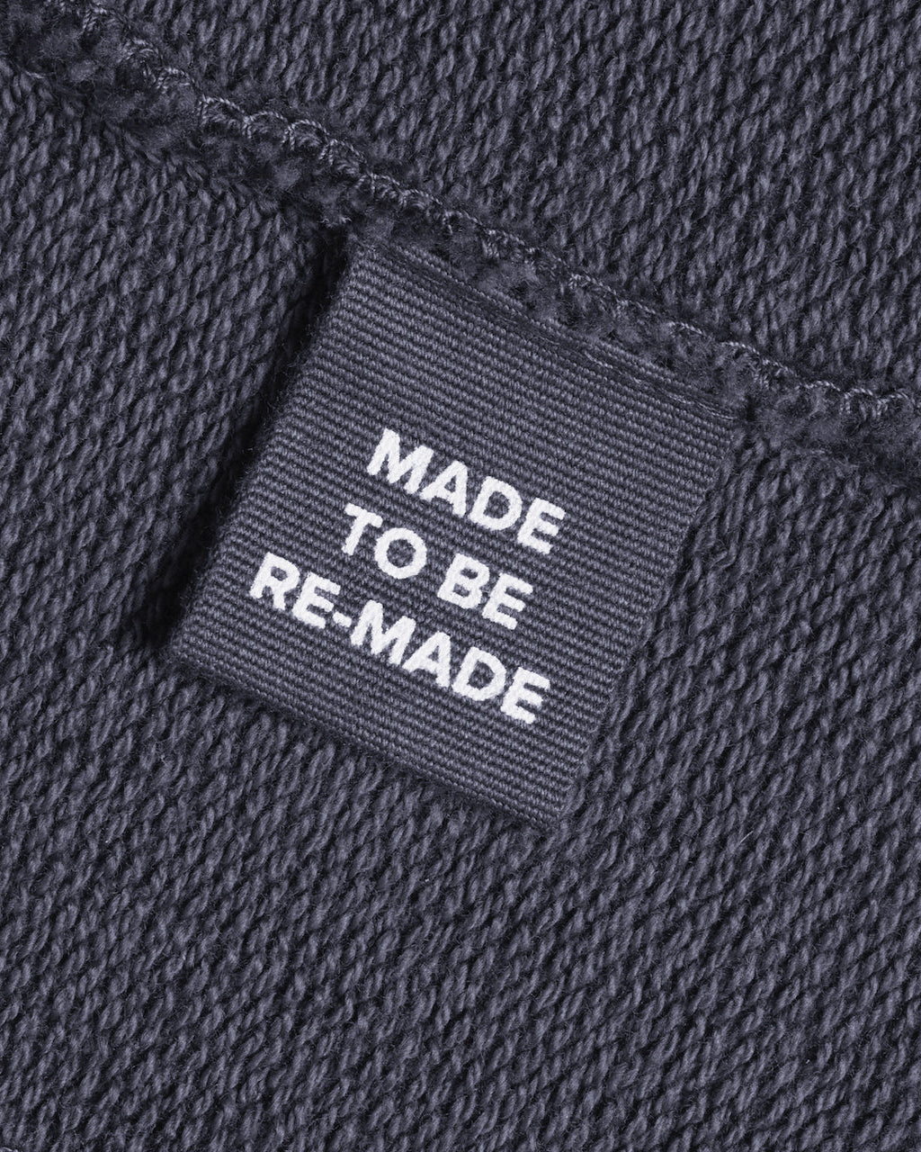 A close up of a label tag in a dark grey organic cotton sweatshirt that says 'made to be re made'.
