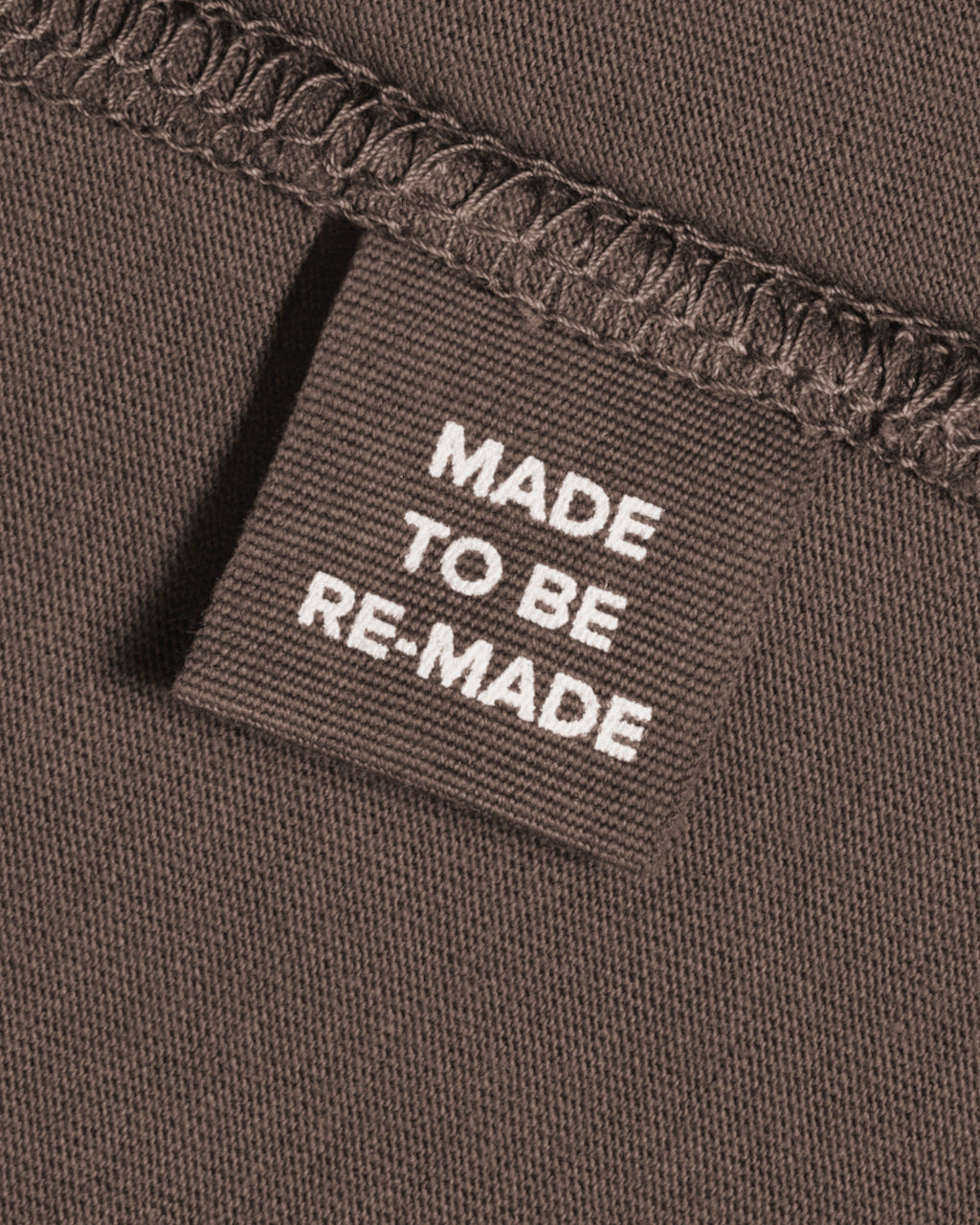 A close up of a label tag in a dark khaki organic cotton t shirt that says 'made to be re made'.