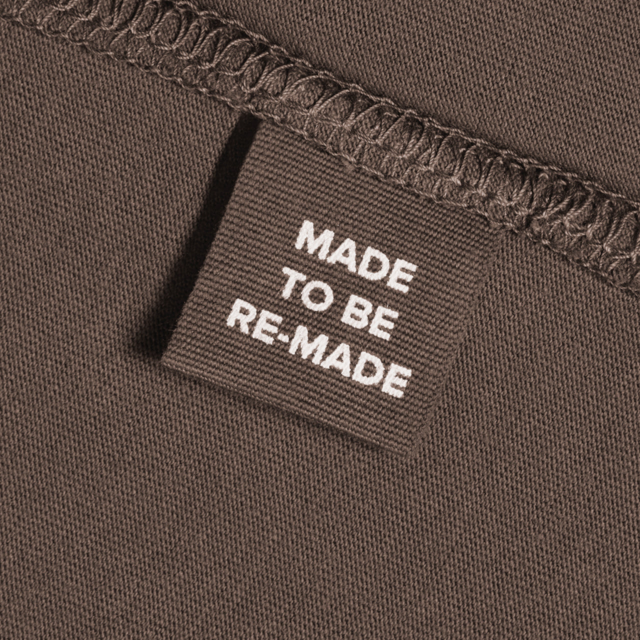 A close up of a label tag in a dark khaki organic cotton t shirt that says 'made to be re made'.