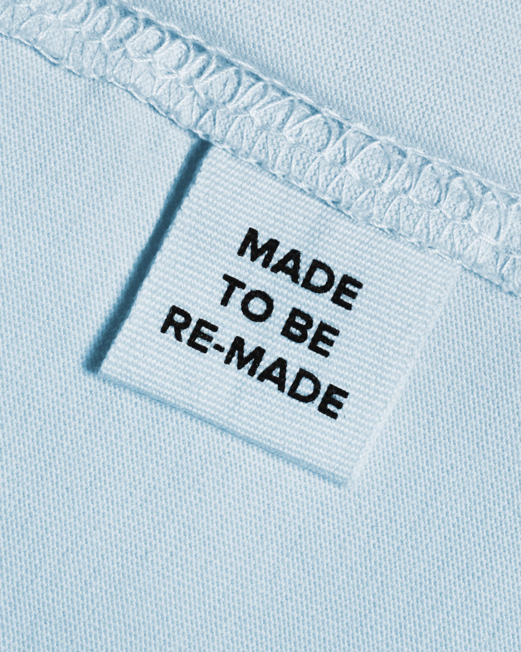 A close up of a label tag in a light blue organic cotton t shirt that says 'made to be re made'.