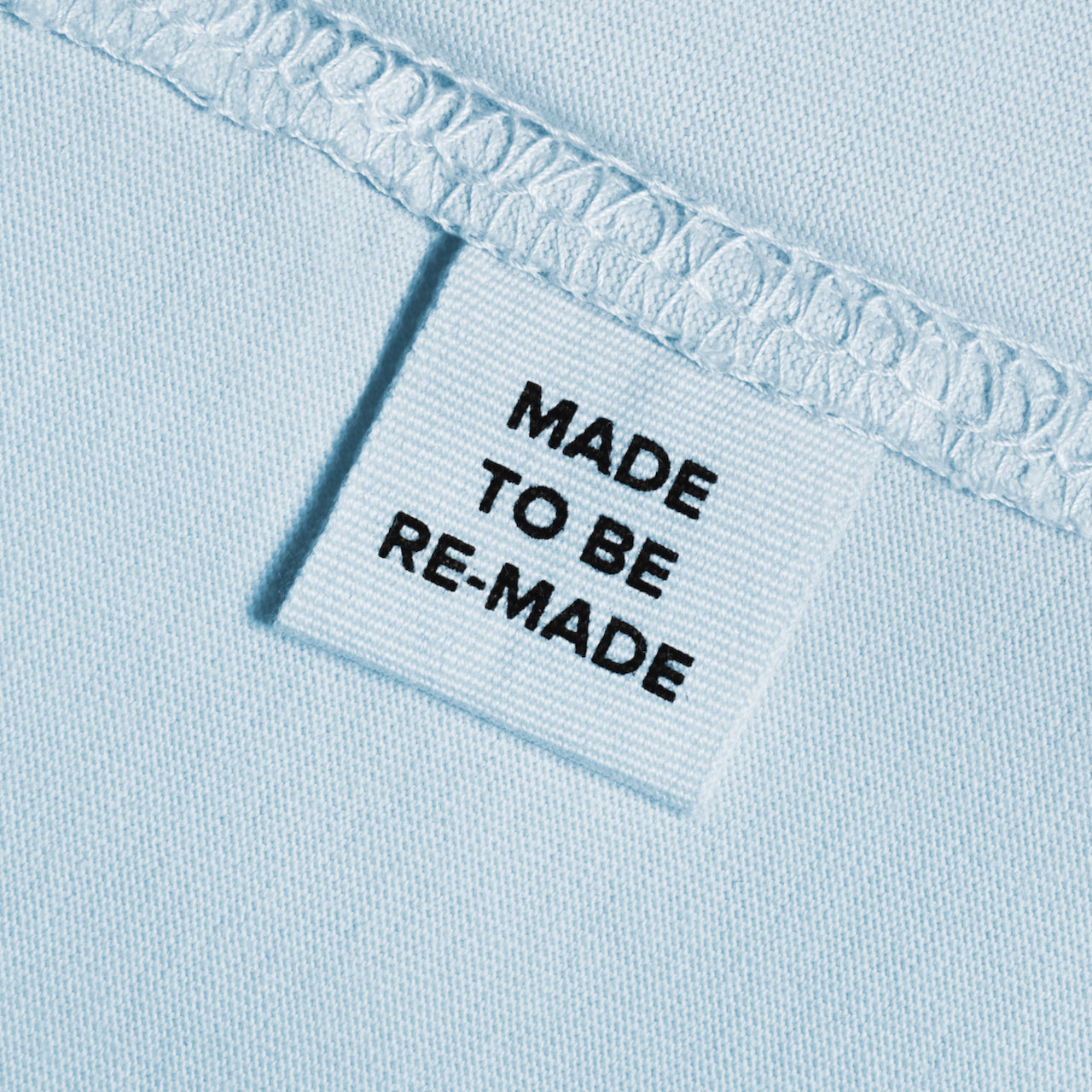 A close up of a label tag in a light blue organic cotton t shirt that says 'made to be re made'.