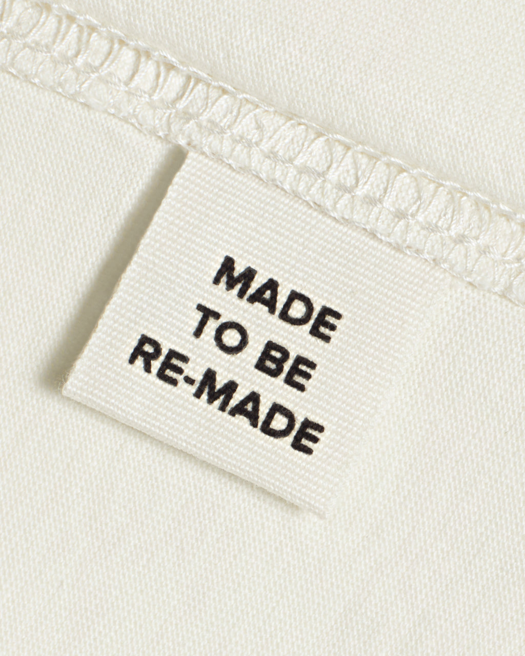 A close up of a label tag in an ecru organic cotton t shirt that says 'made to be re made'.