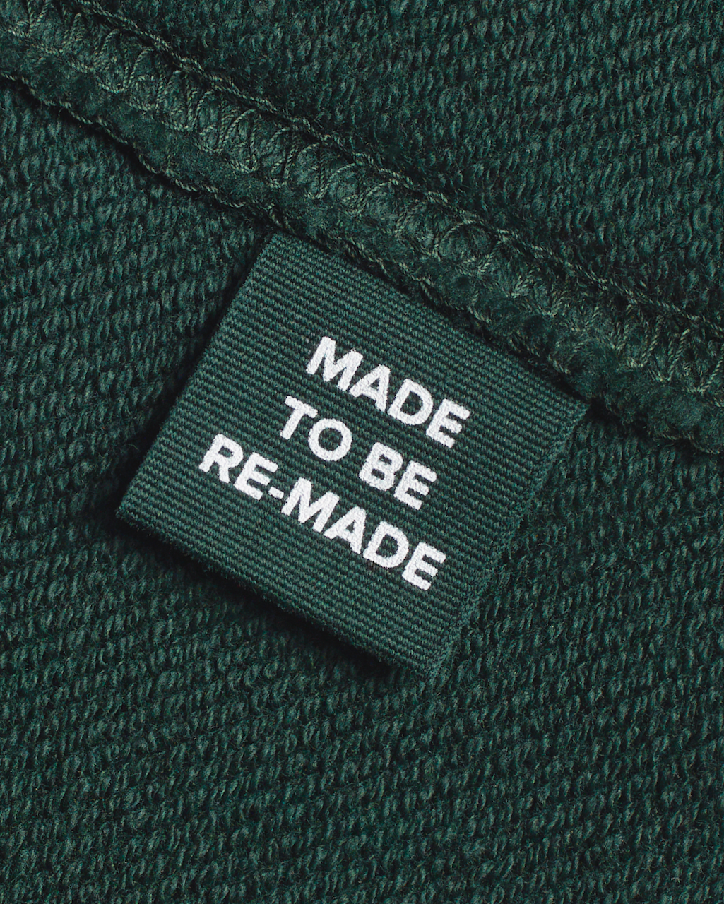A close up of a label tag in a green, organic cotton sweatshirt that says 'made to be re made'.