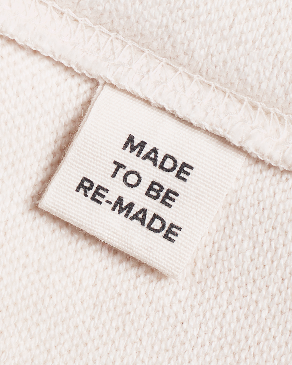 A close up of a label tag in a natural coloured, organic cotton sweatshirt that says 'made to be re made'.