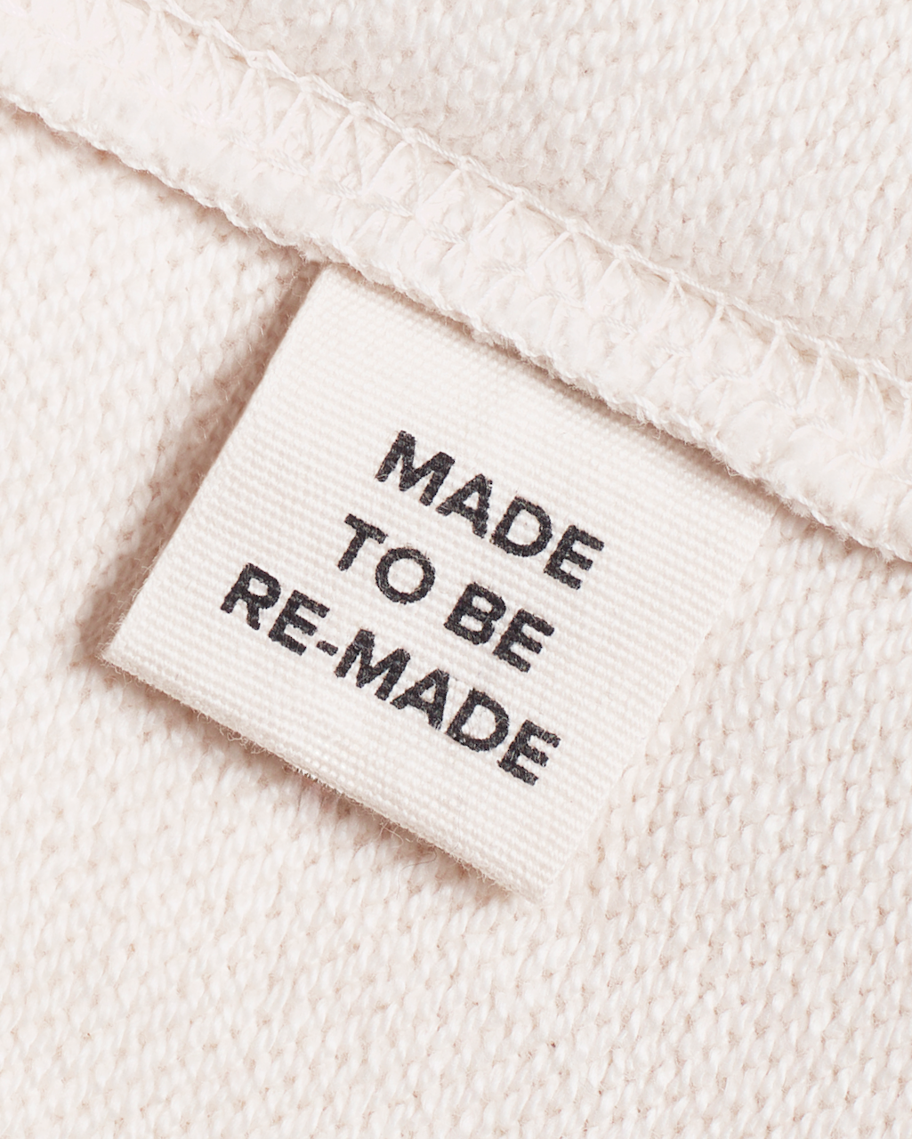 A close up of a label tag in a natural coloured, organic cotton sweatshirt that says 'made to be re made'.