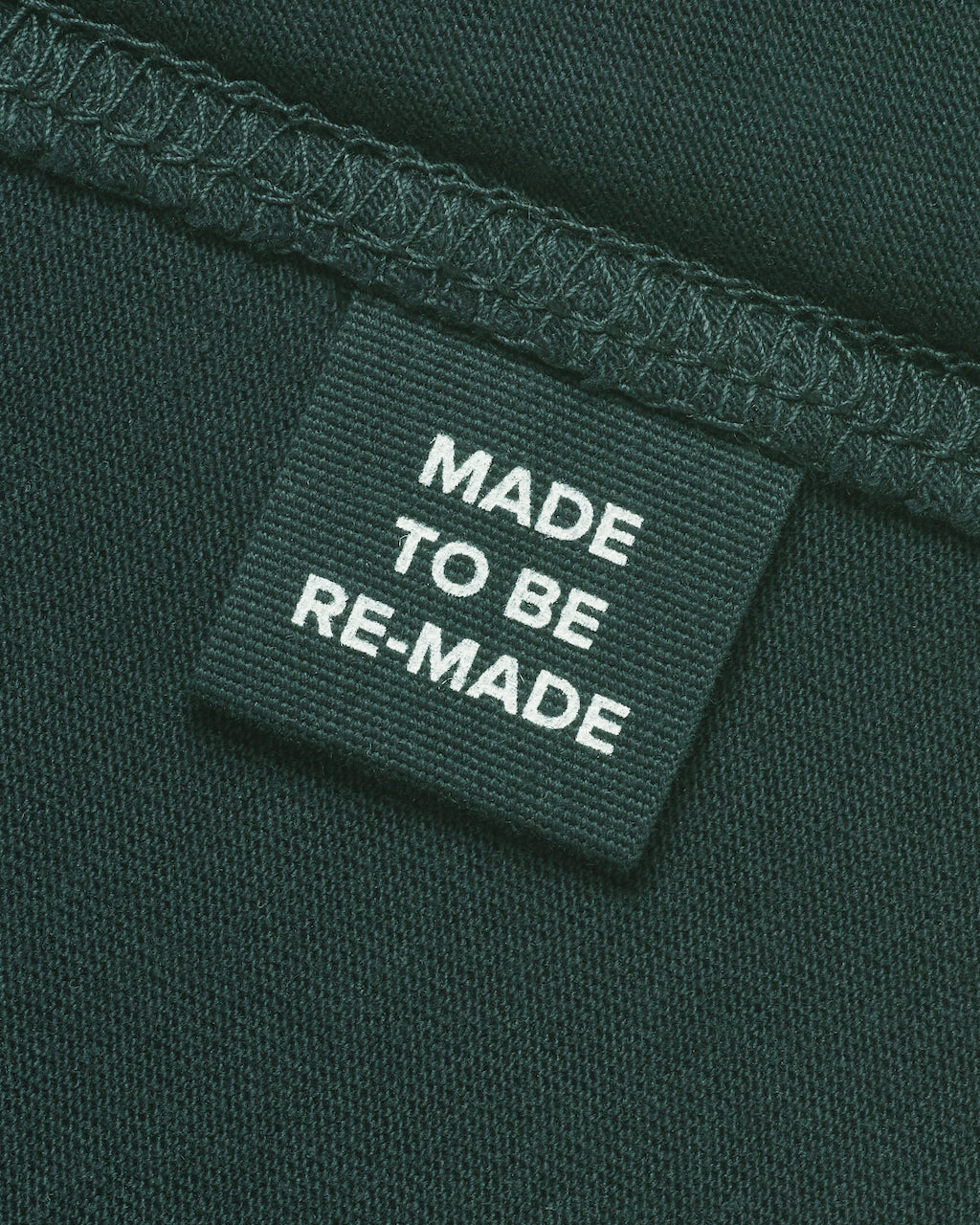 A close up of a label tag in a green organic cotton t shirt that says 'made to be re made'.