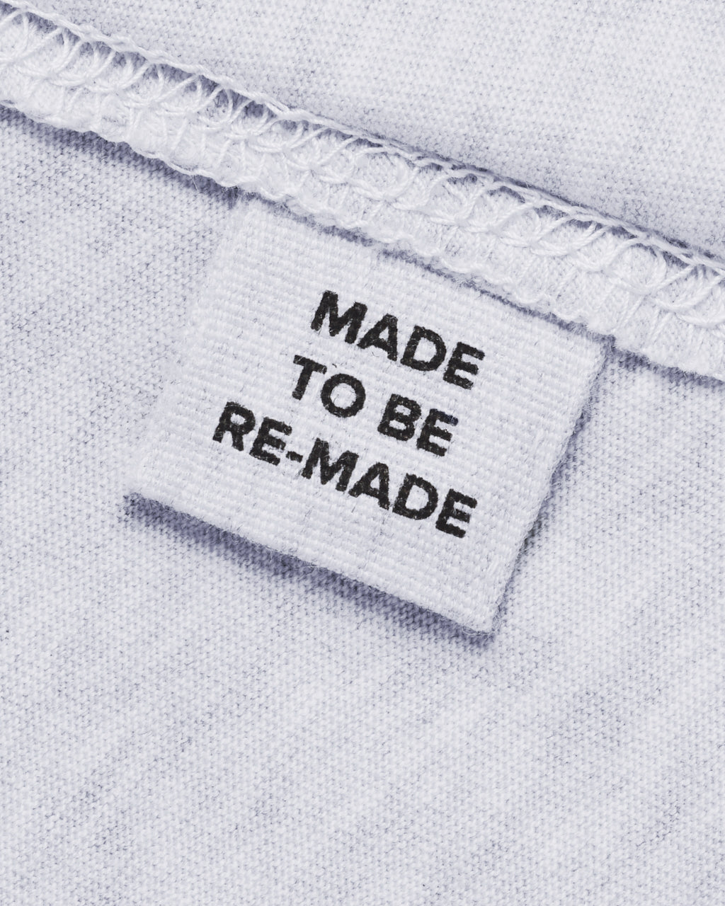 A close up of a label tag in a grey organic cotton t shirt that says 'made to be re made'.