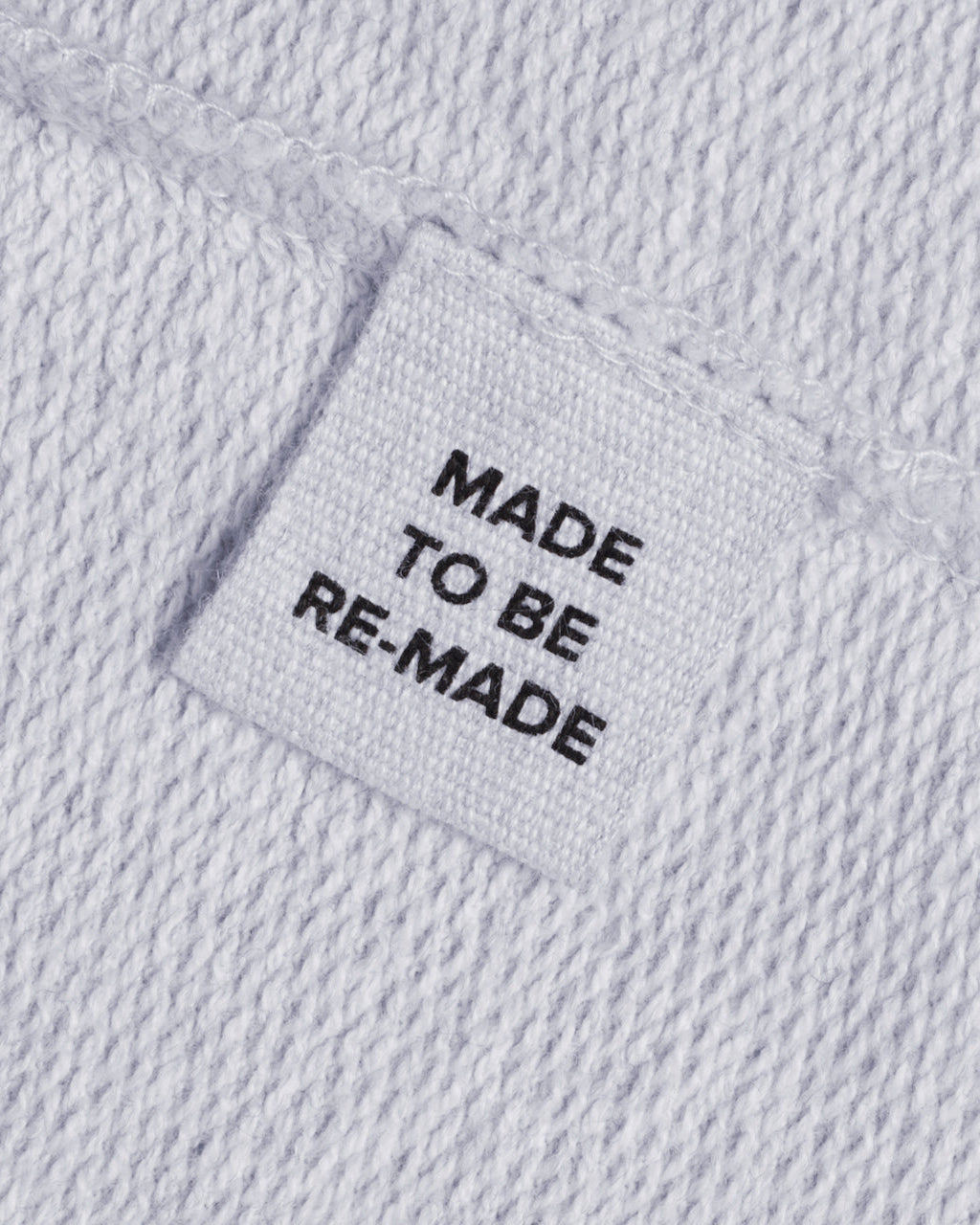 A close up of a label tag in a grey organic cotton sweatshirt that says 'made to be re made'.