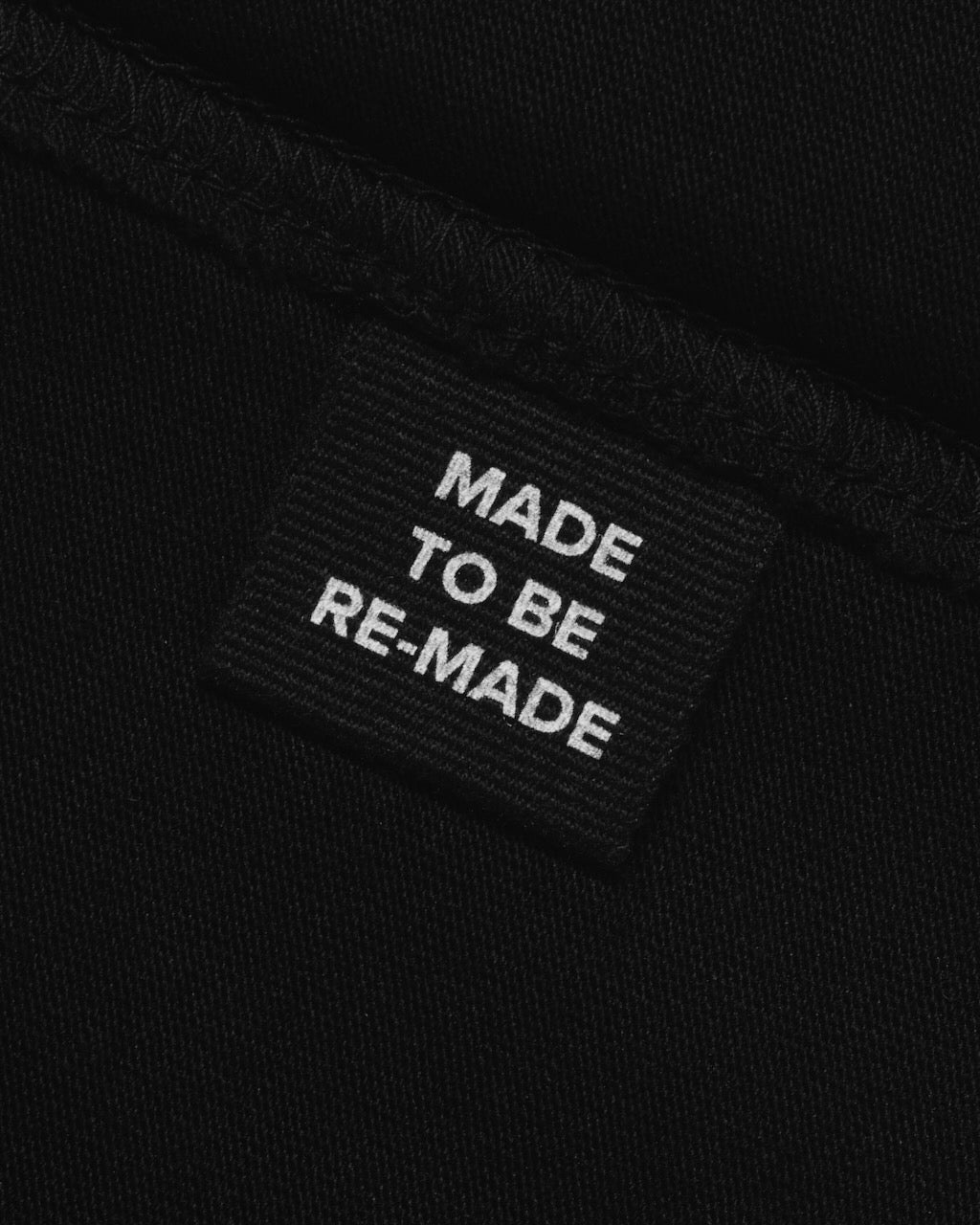 A close up of a label tag in a black organic cotton hoodie that says 'made to be re made'.