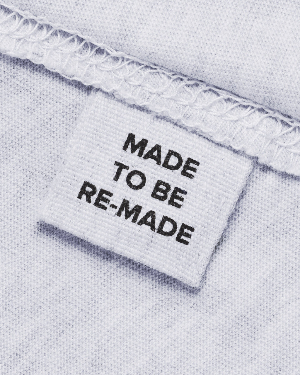 A close up of a label tag in a grey organic cotton hoodie that says 'made to be re made'.